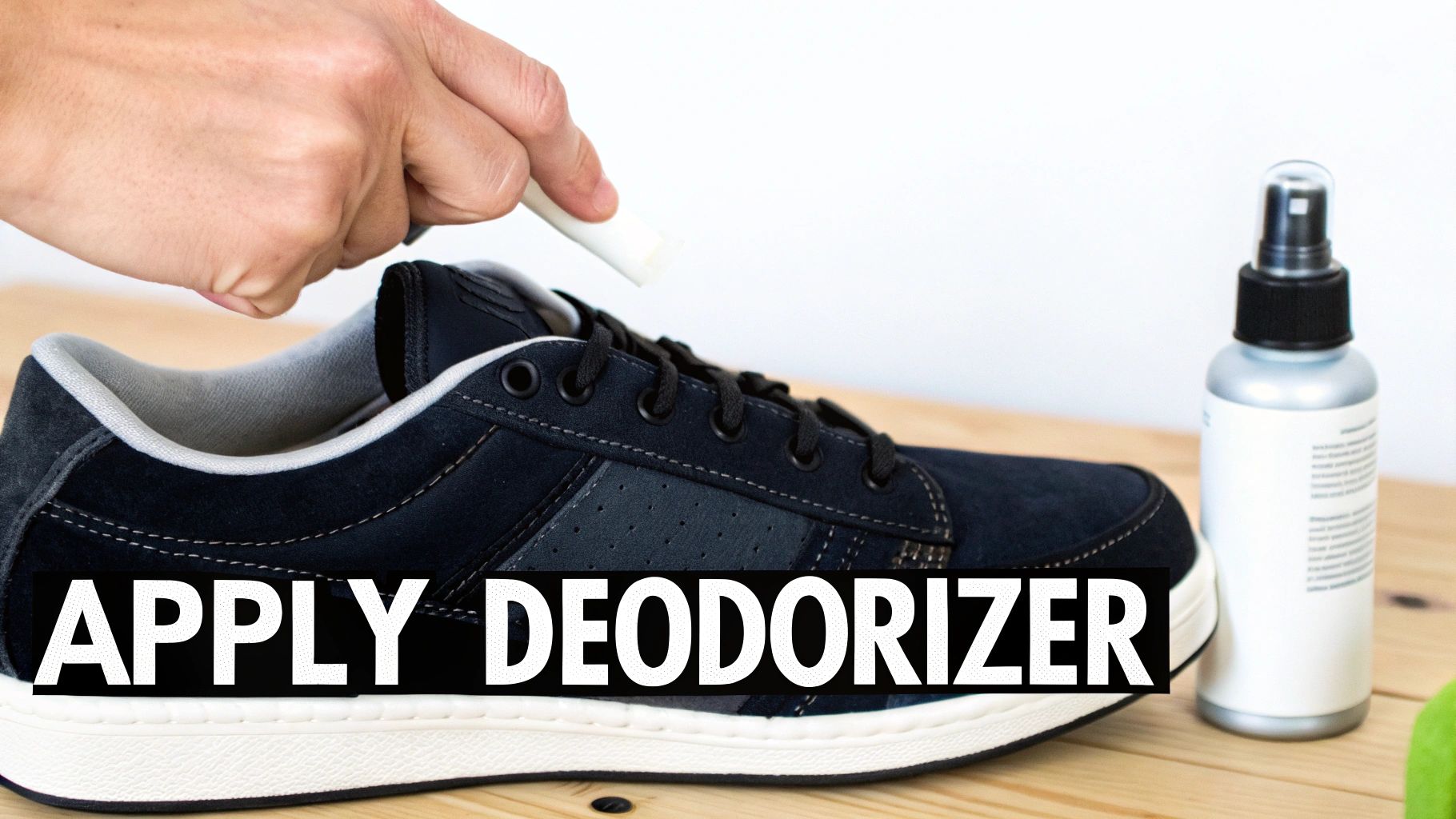 A person's hand applies a stick deodorizer to a dark blue shoe, with a spray bottle nearby.