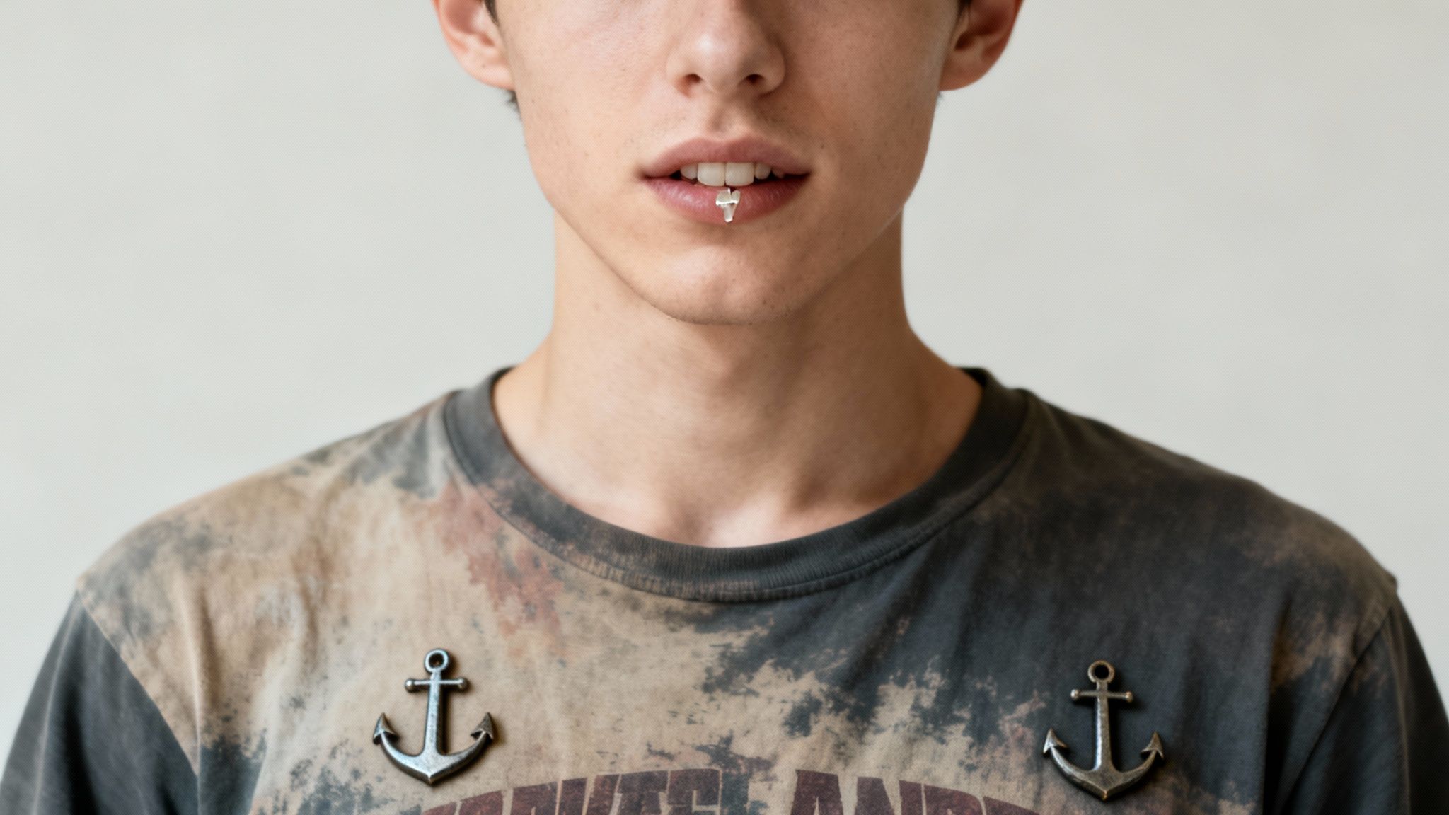 Close-up of a person with a white tooth gem and two anchor pins on a distressed t-shirt.