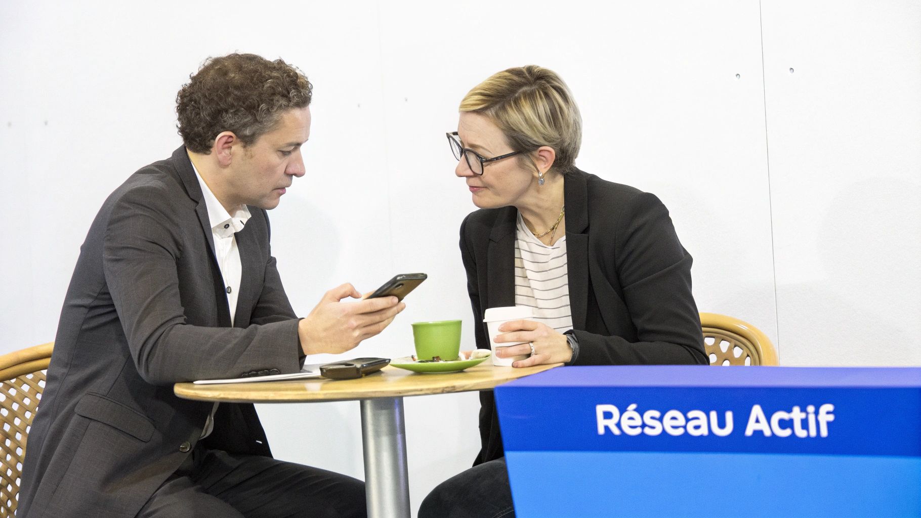 Deux professionnels s'engagent dans une conversation, l'homme regardant son téléphone à côté d'une femme.