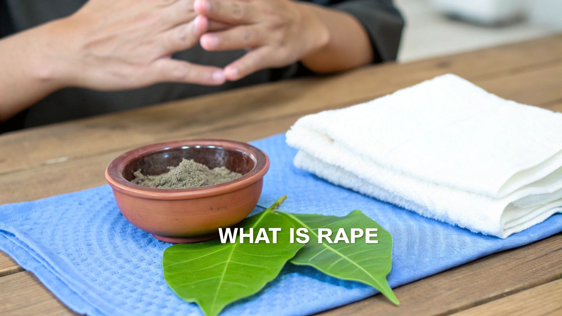 Table with a bowl of powder, green leaves, white towels, and text 'WHAT IS RAPE'.