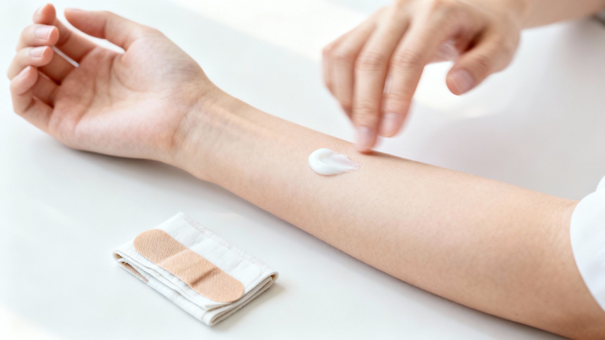A person's arm with a dollop of white lotion being applied, with bandages nearby.