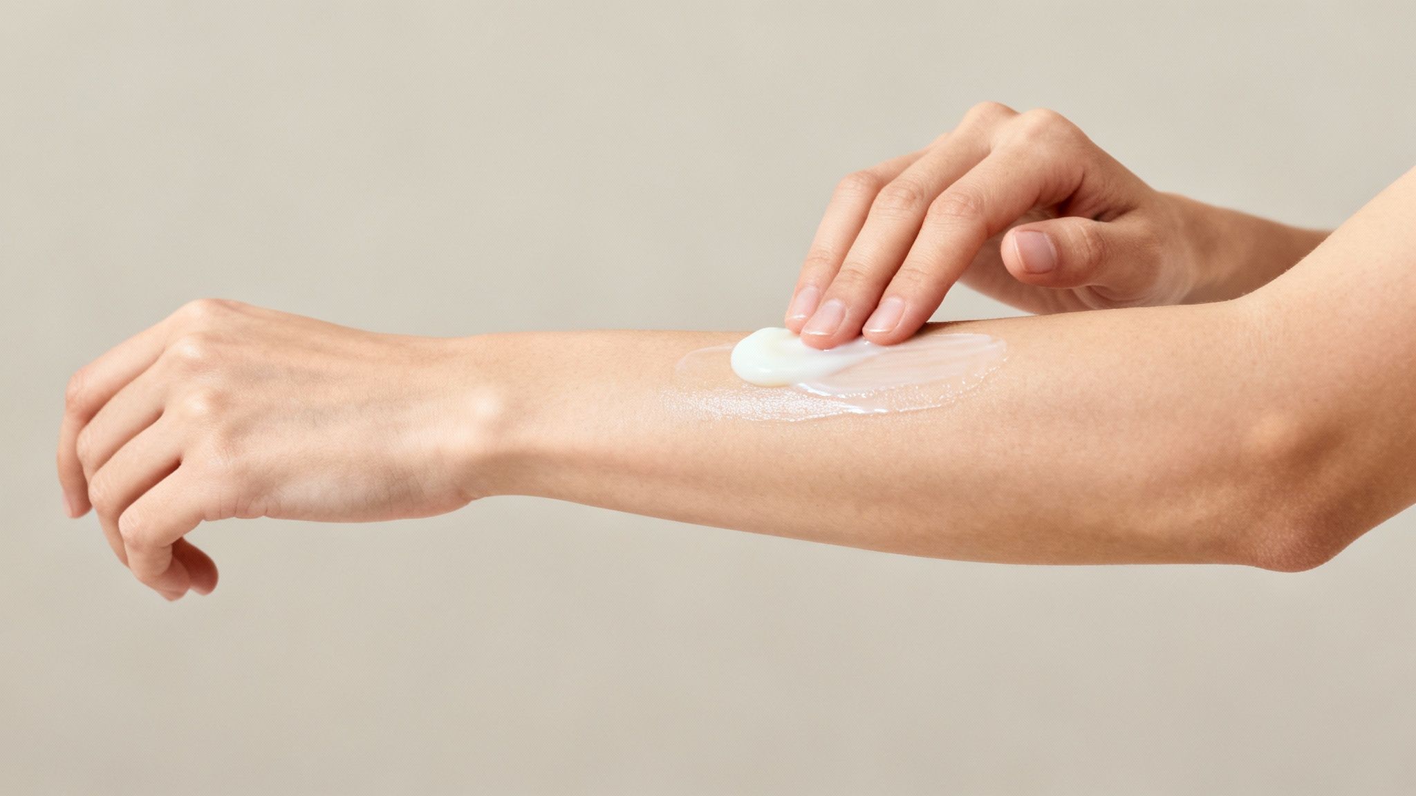 Woman applying white goat milk lotion cream onto forearm with cotton pad for moisturizing skin