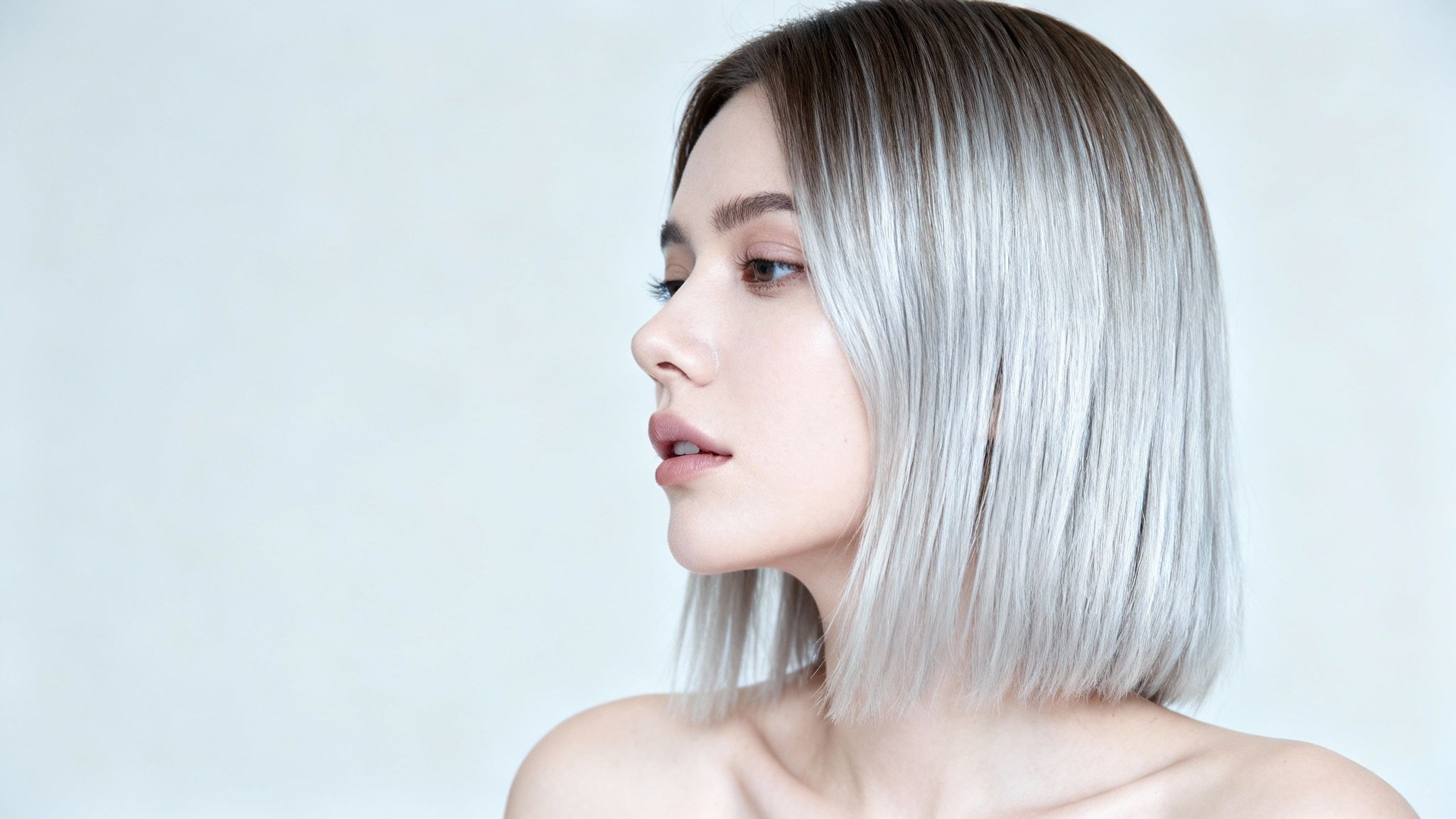 Profile view of a young woman with a modern long bob, dark roots blending to silver-blonde hair.