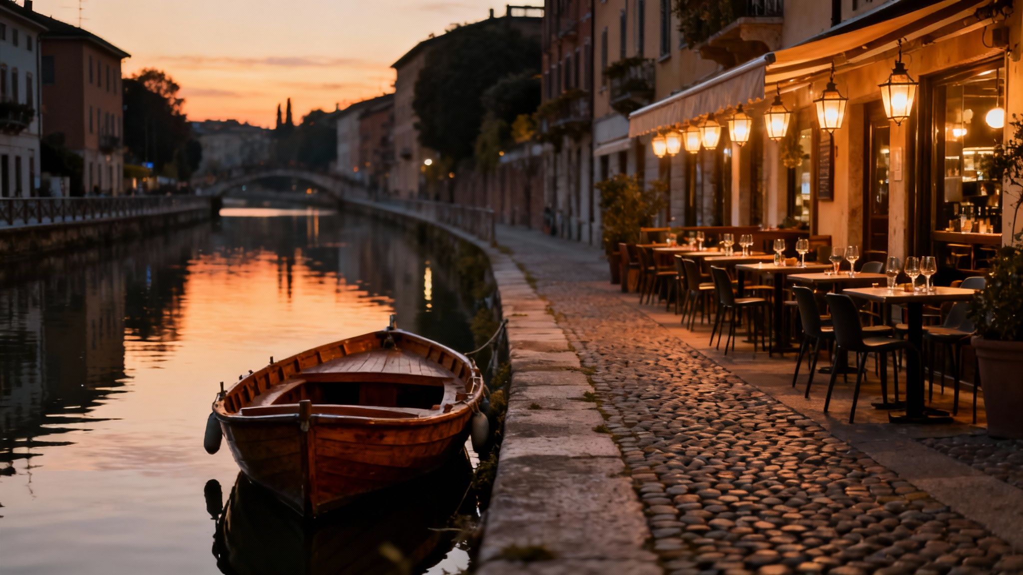 A picturesque canal scene at sunset with a boat, and a charming restaurant with outdoor seating illuminated by lanterns.