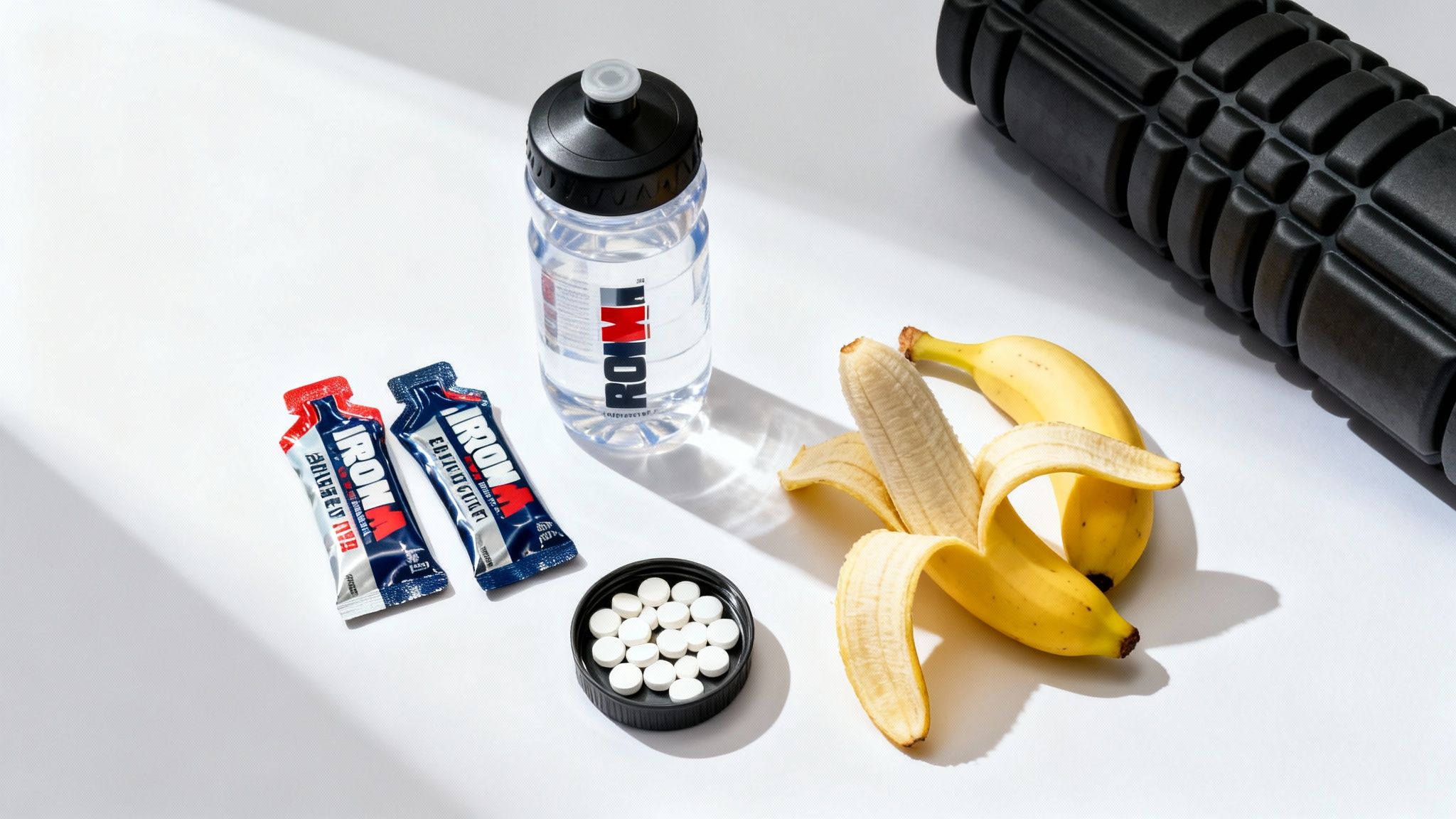 An assortment of Ironman training essentials: water bottle, energy gels, supplements, bananas, and a foam roller.