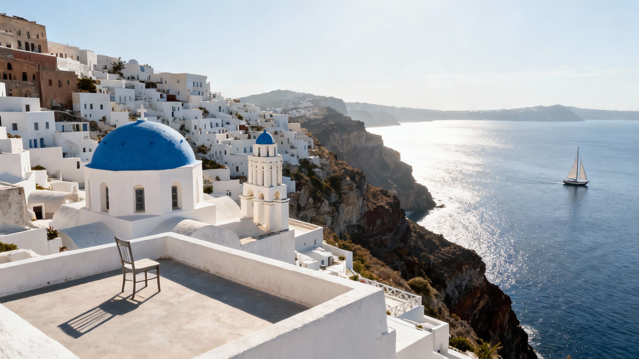 A picturesque view of Santorini, Greece, with white buildings, a blue-domed church, cliffs, and a sailboat on the sparkling sea.