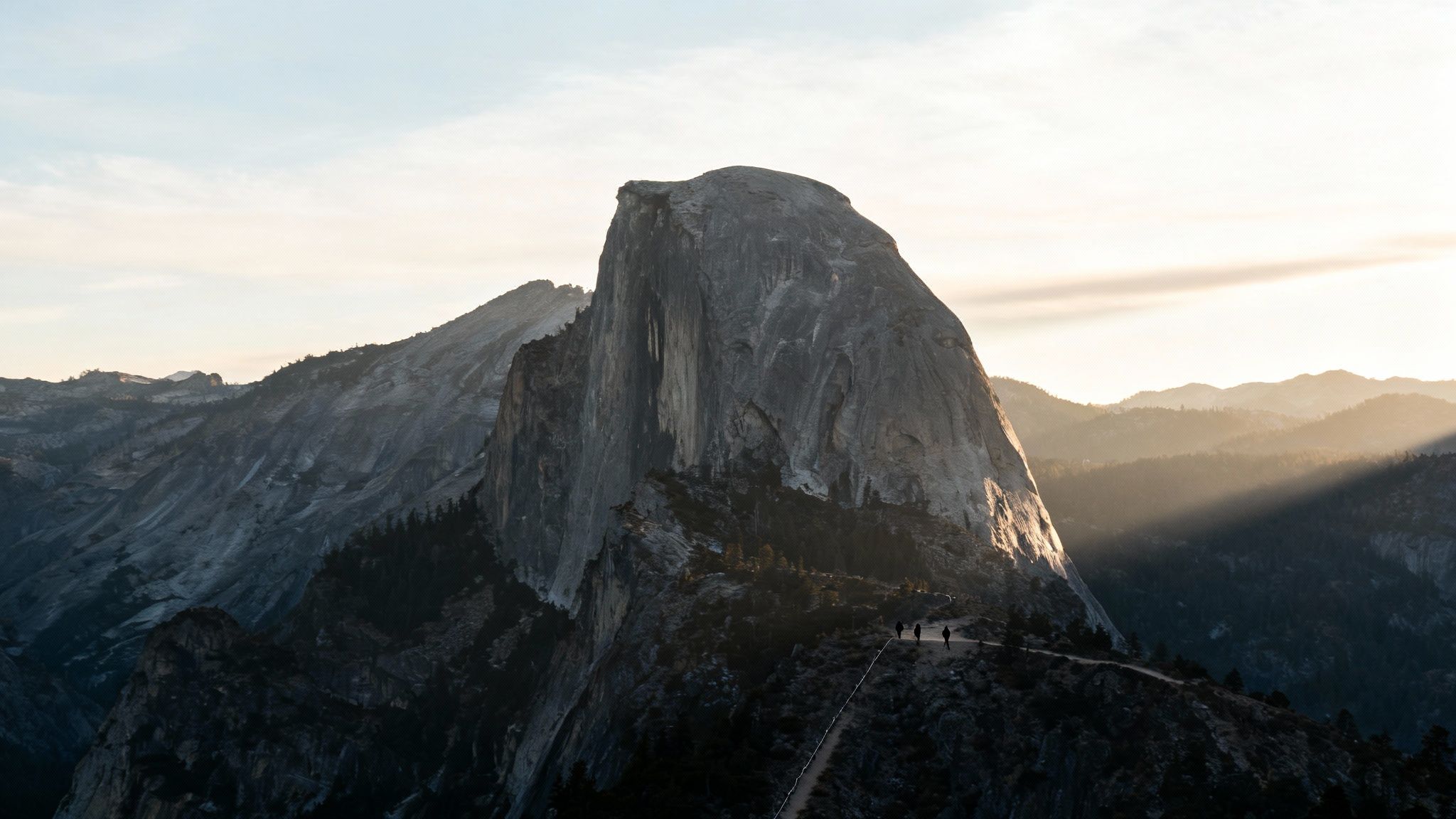 Panoramic view of Half Dome in Yosemite National Park, with hikers on a winding trail under golden light.