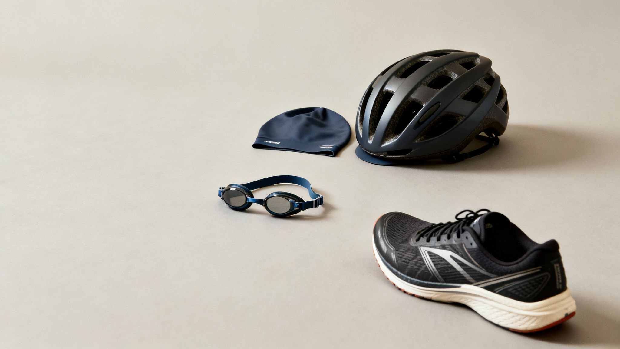 Triathlon training gear including a swim cap, goggles, bike helmet, and running shoes on a grey background.