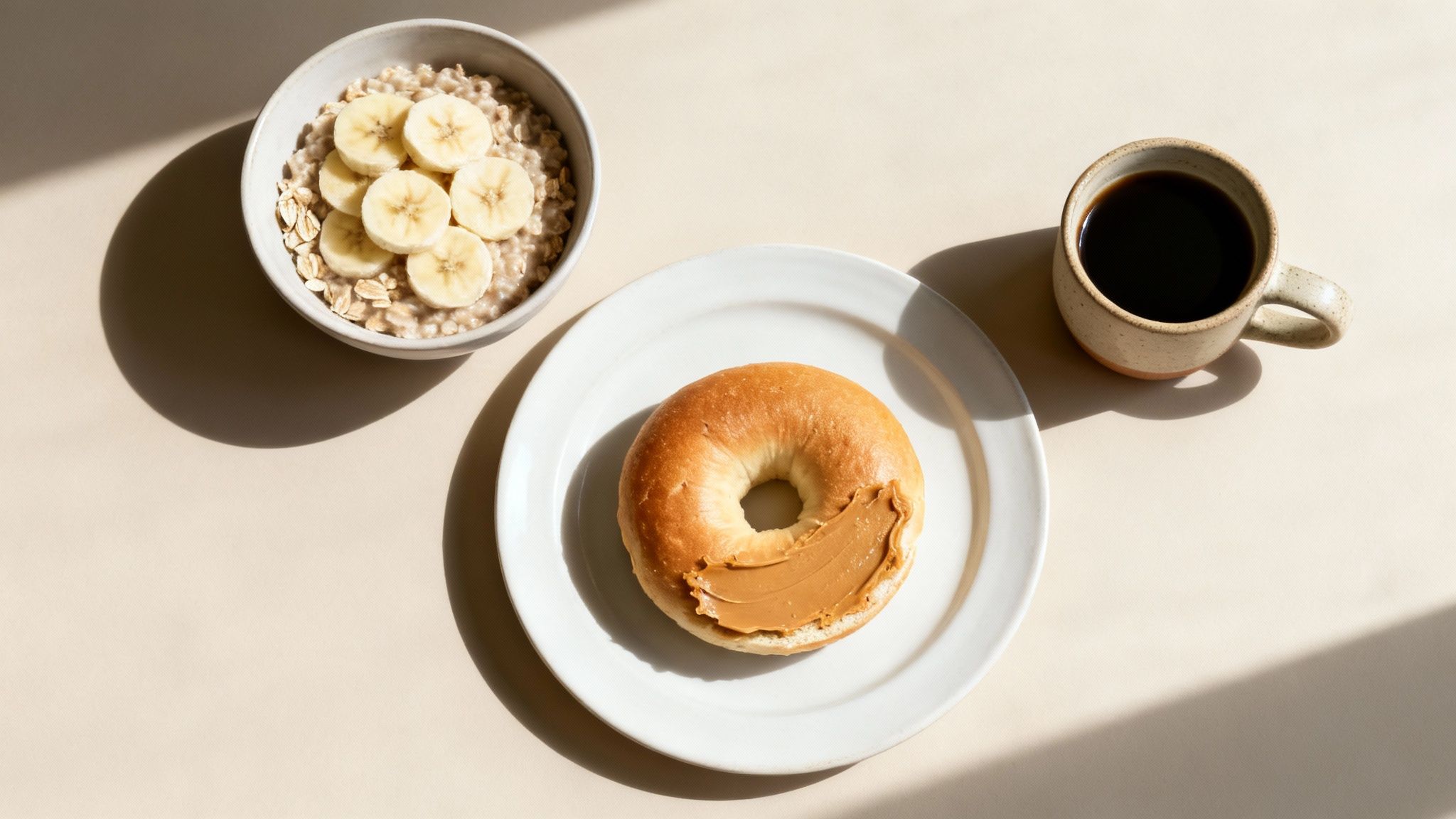 A healthy breakfast spread featuring oatmeal with banana, a bagel with peanut butter, and black coffee.
