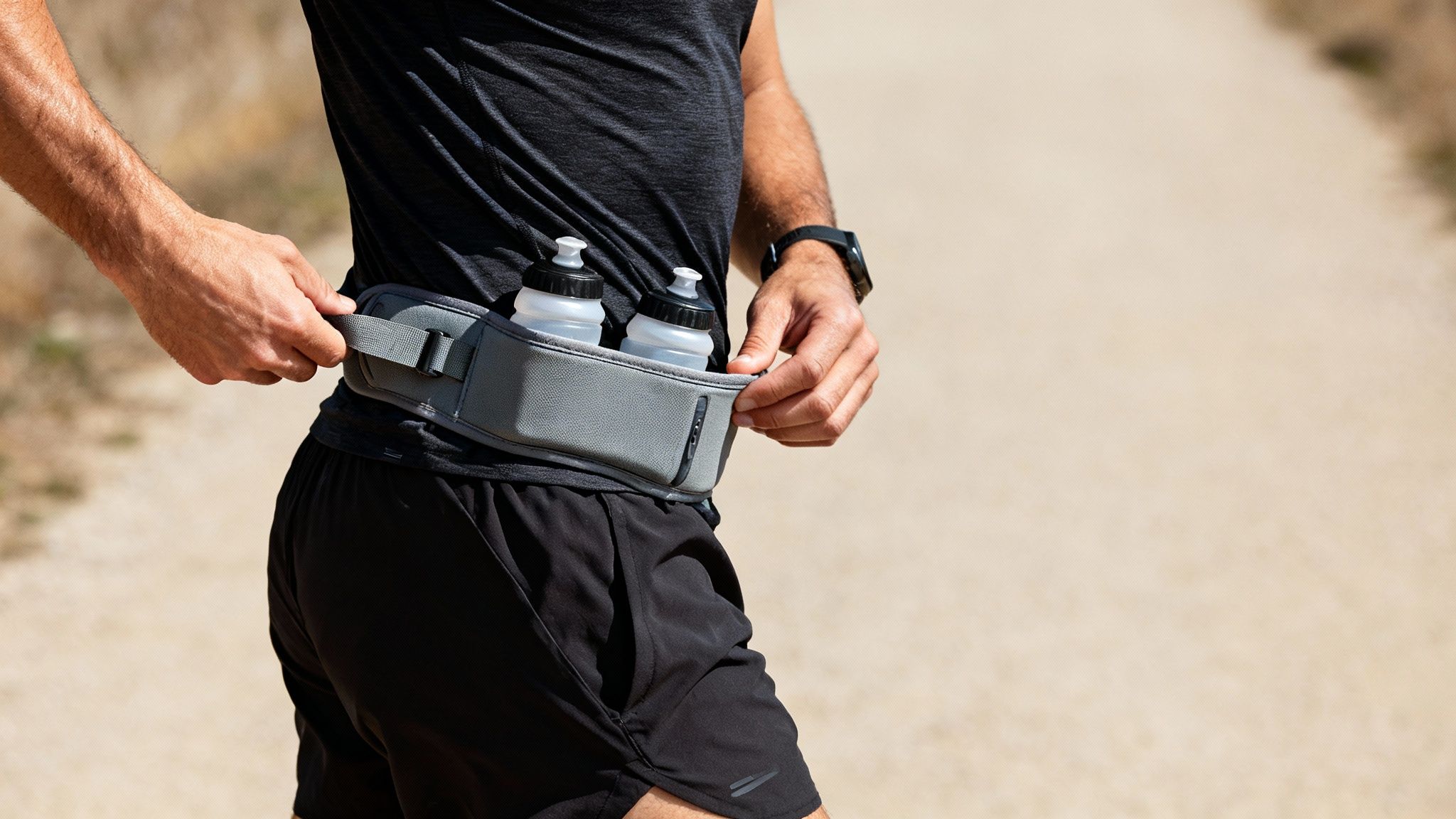 Close-up of a runner adjusting a grey hydration belt with two water bottles.