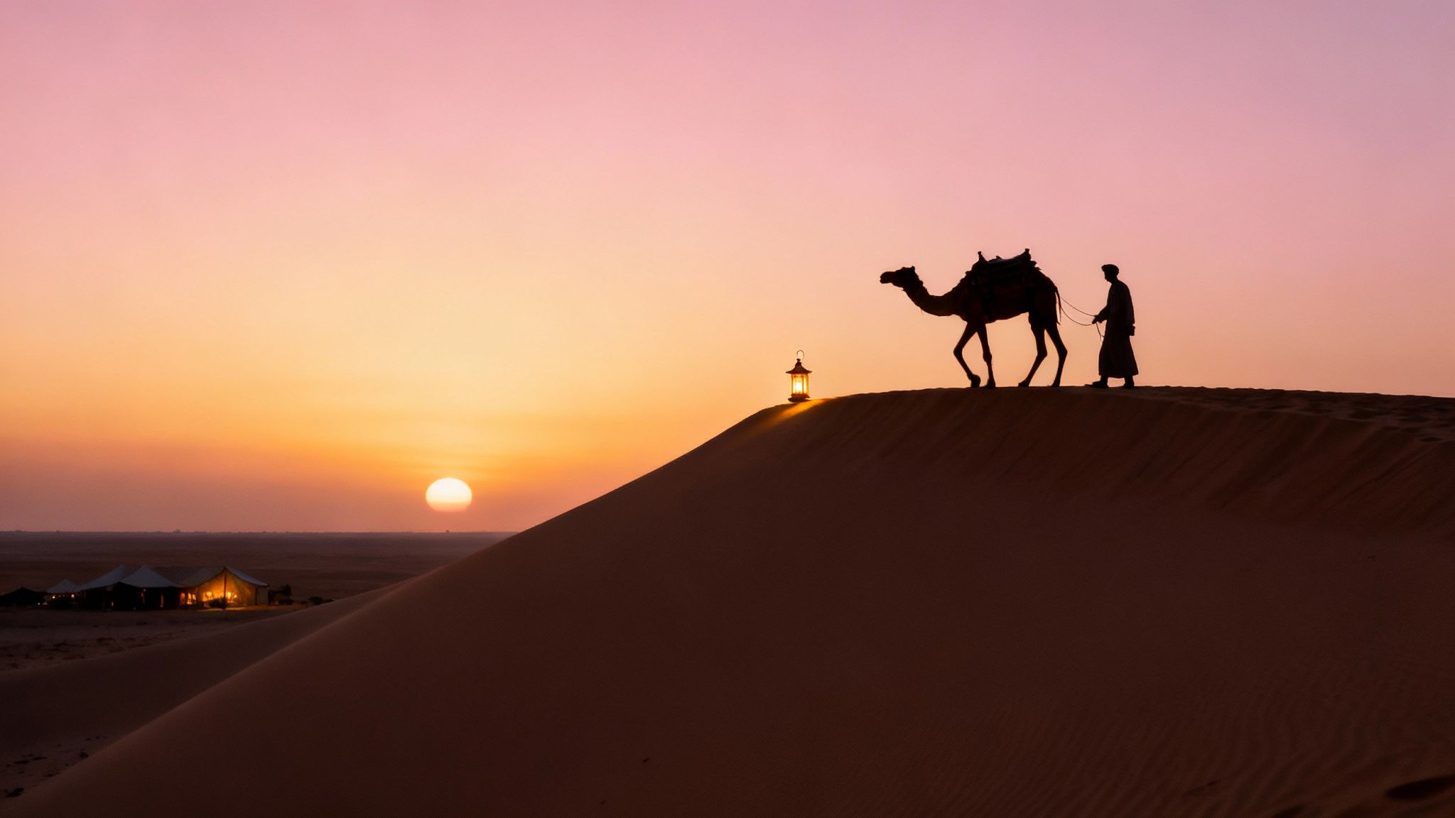 Silhouette of camel and guide walking on desert sand dune at sunset in Dubai
