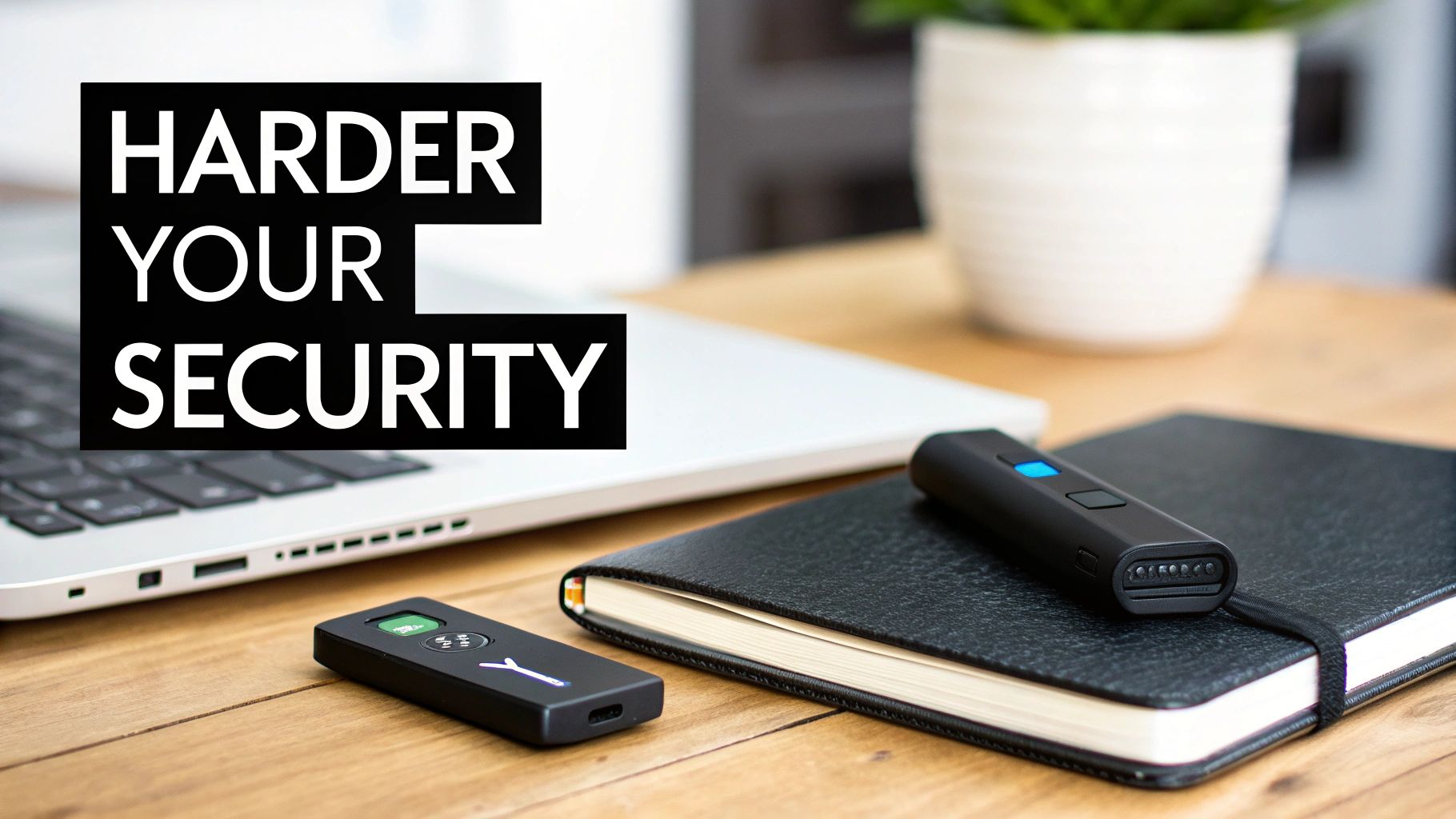 Two black security keys on a wooden desk with a laptop, notebook, and a potted plant.