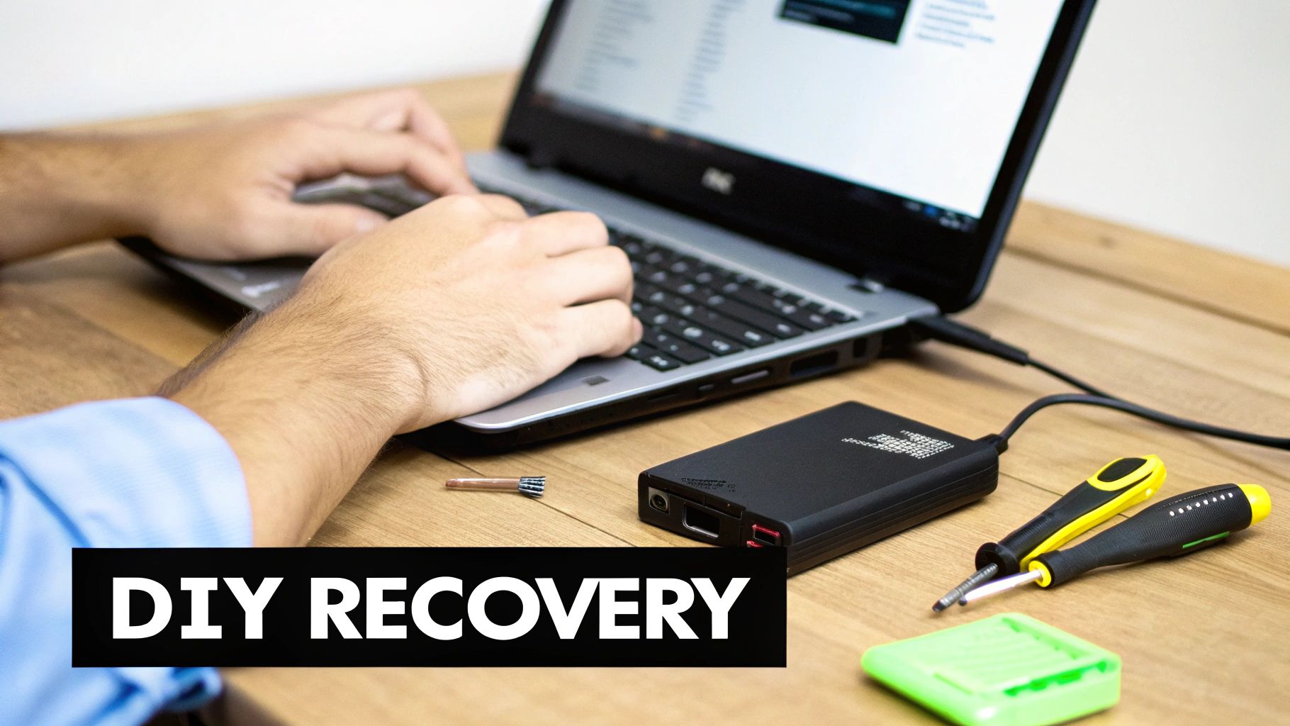 A person is typing on a laptop with data recovery tools and an external hard drive on a wooden desk.