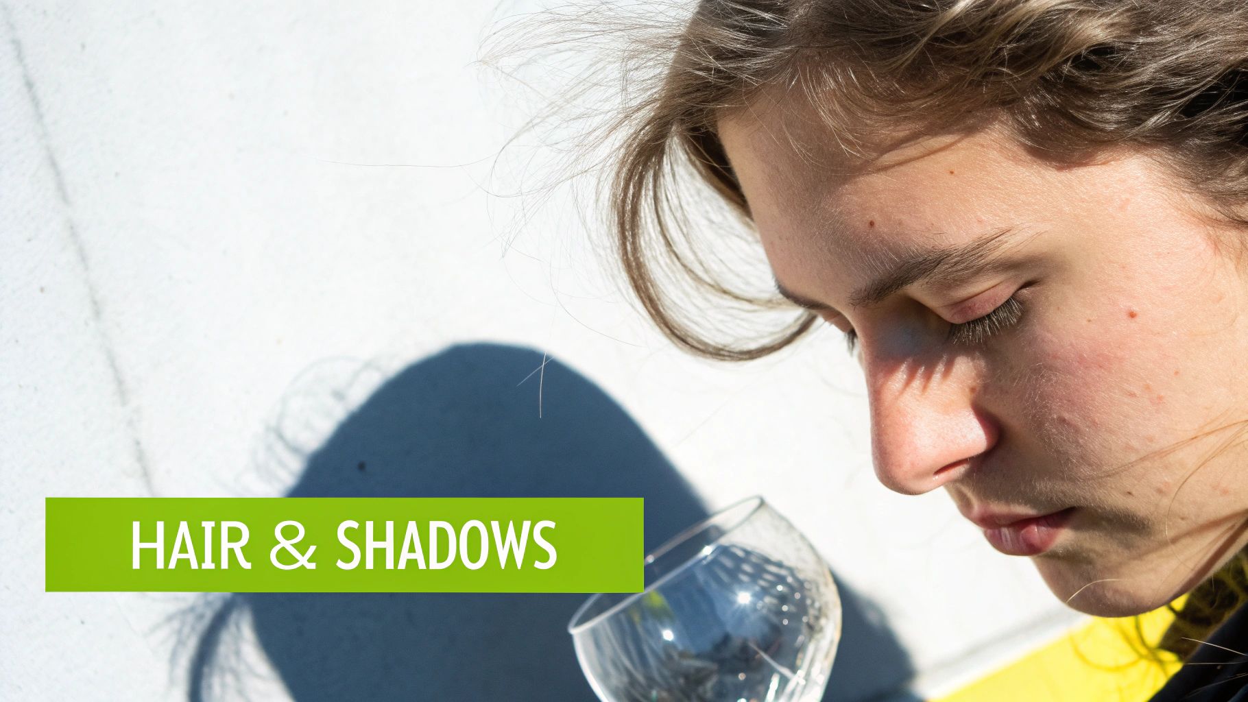 Close-up of a person's profile with hair blowing and strong shadows on their face and the white wall.