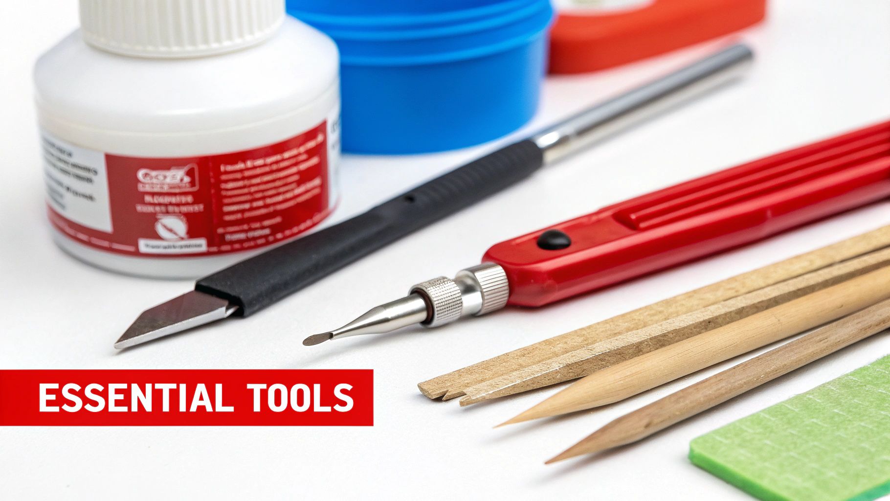A close-up of essential modeling tools like a hobby knife, sprue cutters, and sanding sticks laid out on a cutting mat next to a model kit.