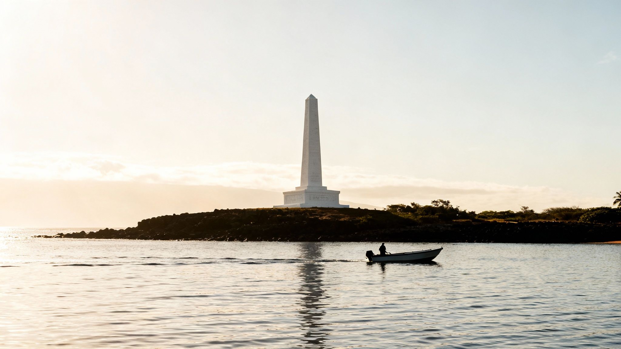 A white obelisk monument stands on a rocky island with a boat and person in the water below.