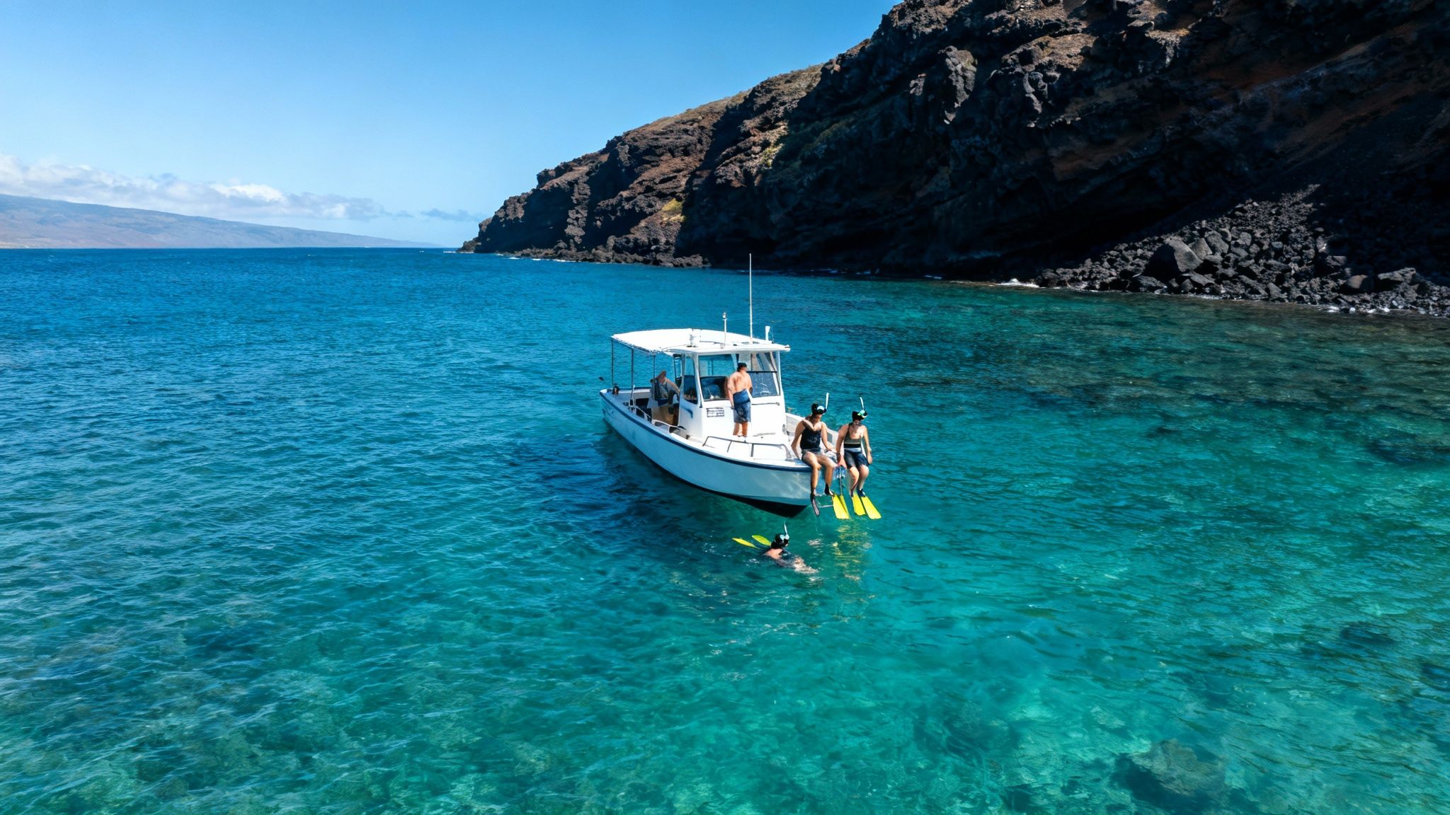 A boat with snorkelers in clear blue water next to a rocky Hawaiian coast under a sunny sky.