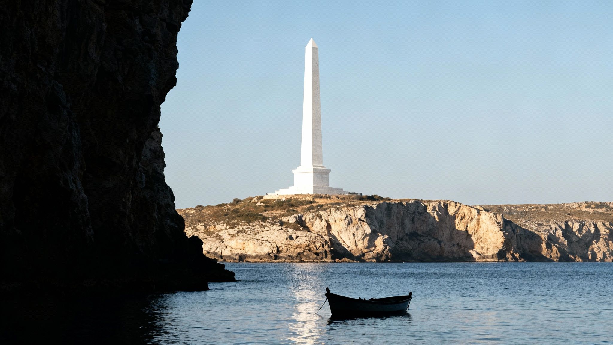 A tall white obelisk stands on a rocky cliff overlooking a calm sea with a small boat.