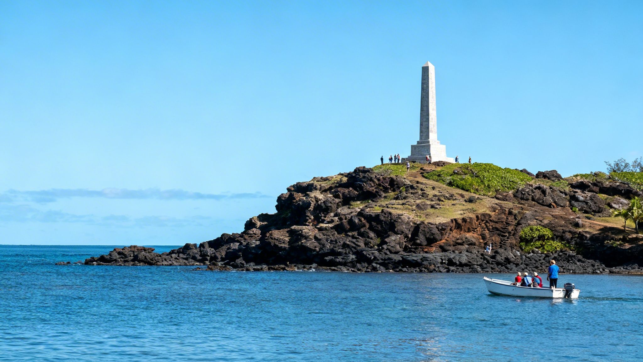 A tall white obelisk monument stands on a rocky headland overlooking the blue ocean. A small boat carrying people floats nearby.