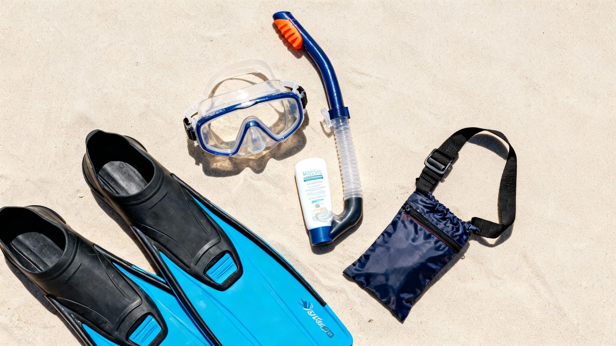 Snorkeling gear, including flippers, mask, snorkel, sunscreen, and a bag, laid on sandy beach.