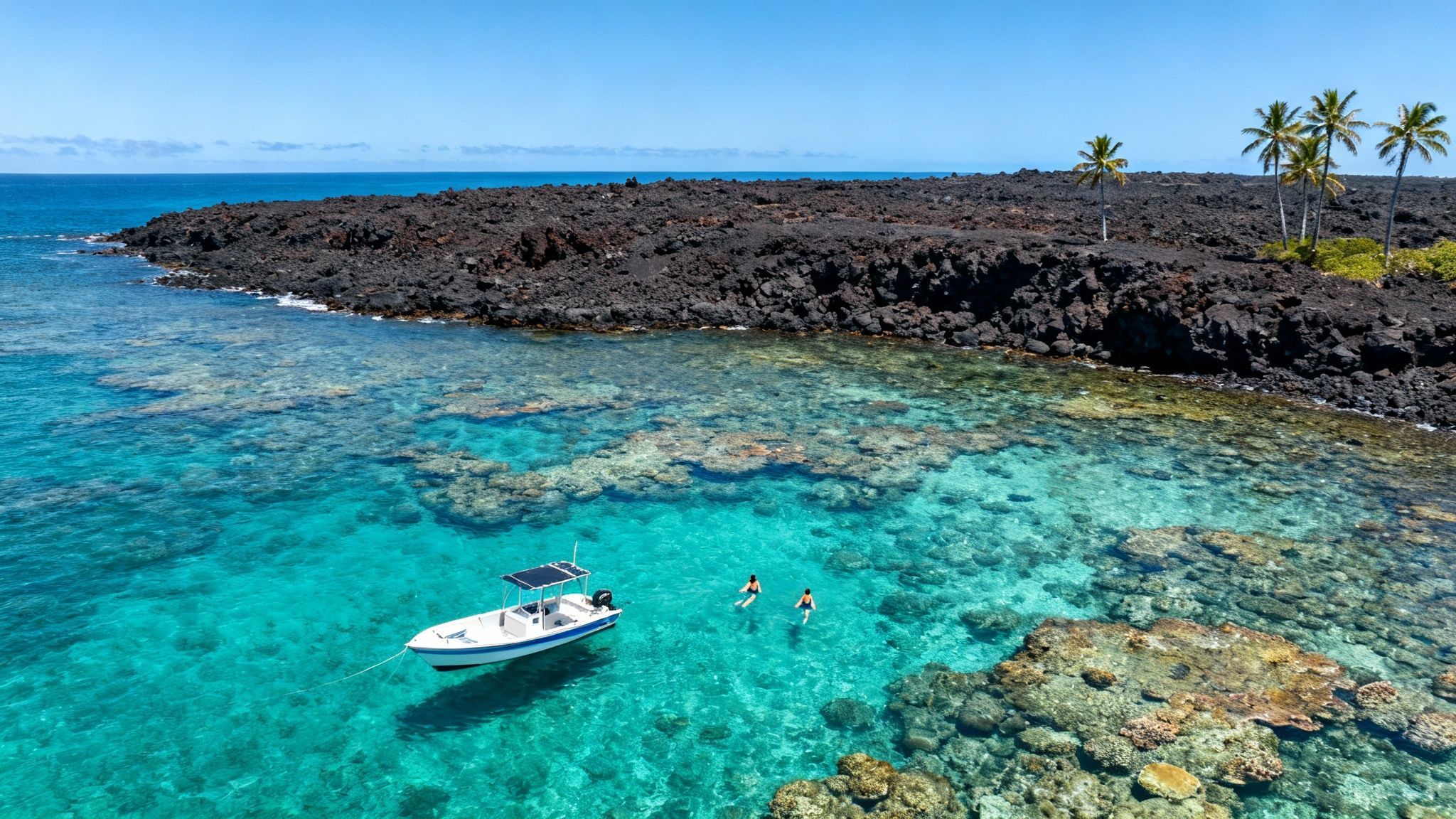 Aerial view of clear turquoise water, volcanic coastline, a boat, and two snorkelers in a tropical paradise.