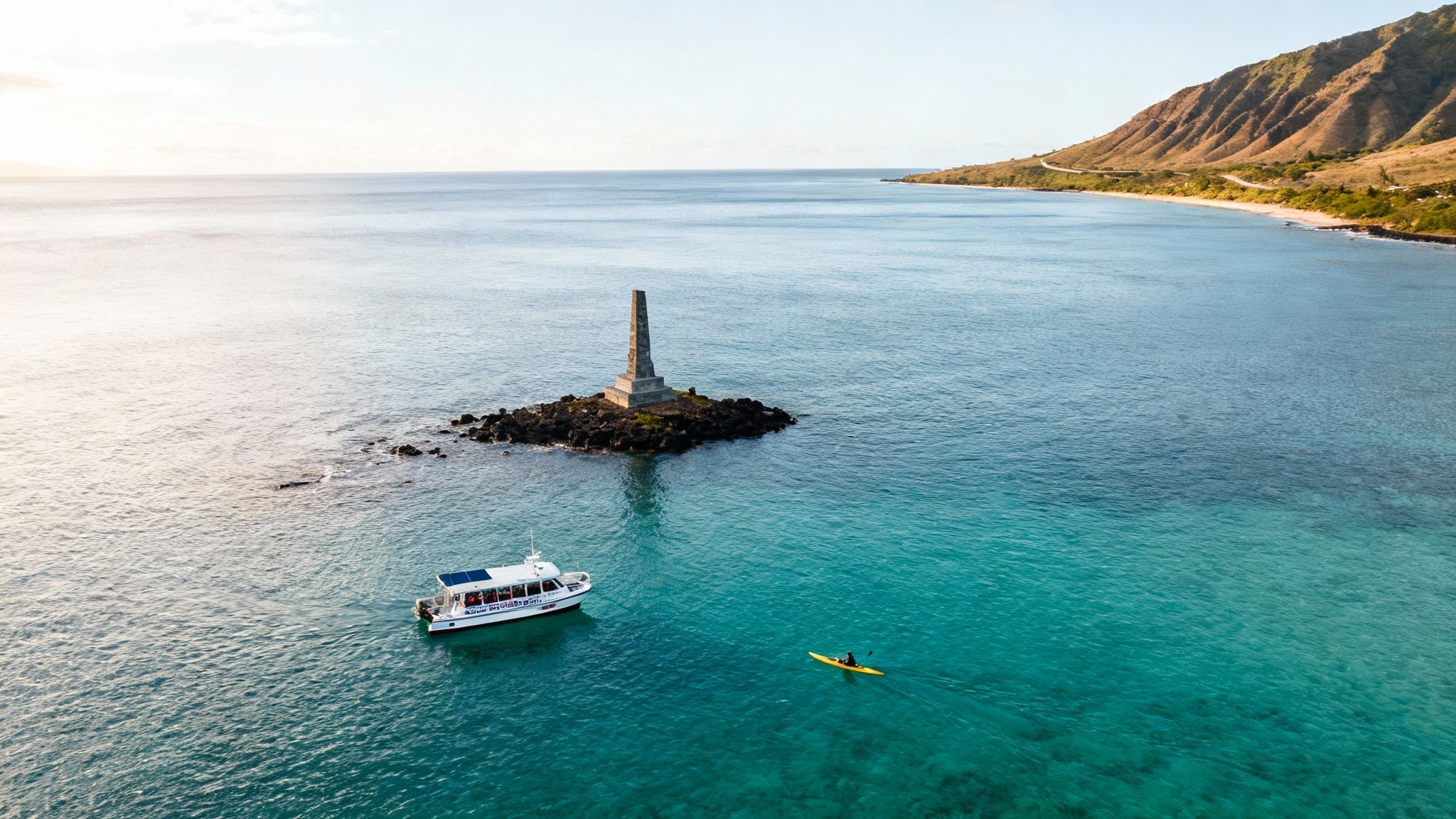 Aerial shot of Captain Cook Bay with a monument, tour boat, kayaker, and scenic coastline.