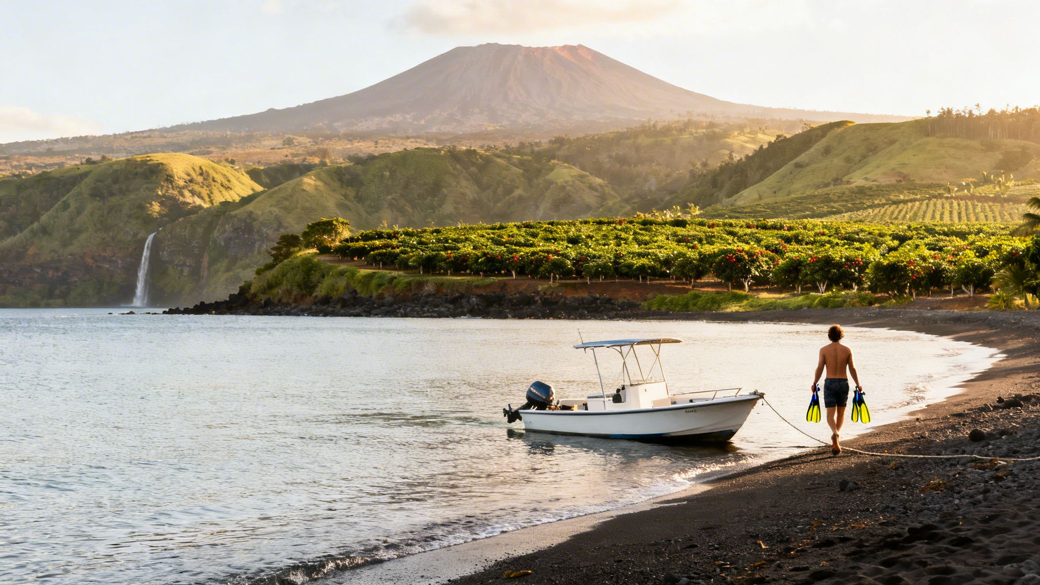 Man with snorkeling fins walks on a black sand beach towards a boat with a volcano and waterfall in the background.