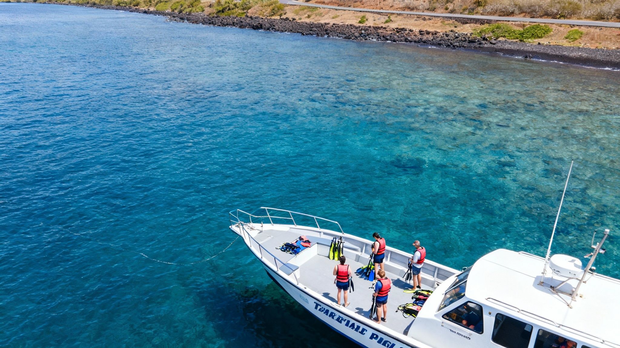 Aerial view of people on a boat preparing to snorkel in clear blue Hawaiian waters.