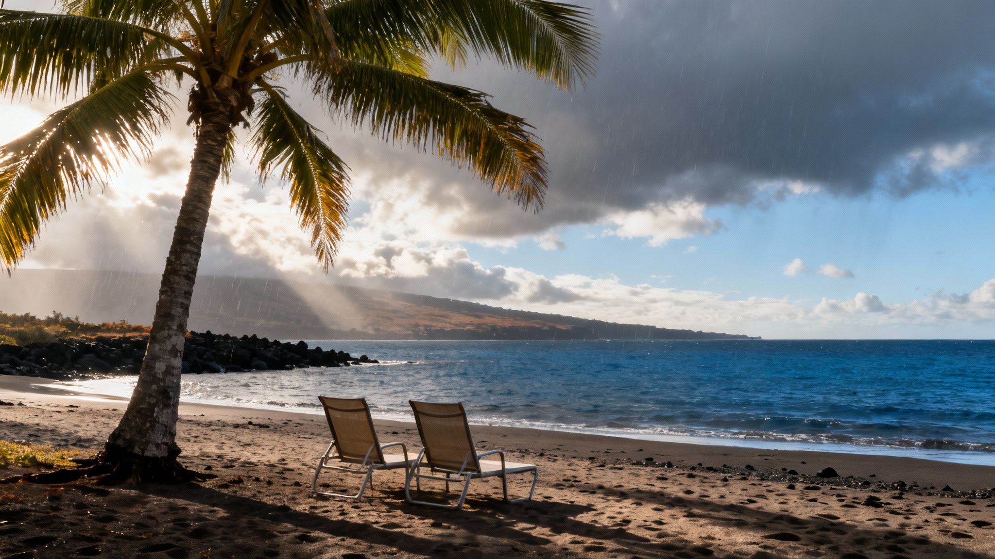 A tropical beach scene with a palm tree, two empty chairs, ocean, and mountains under a sunshower.