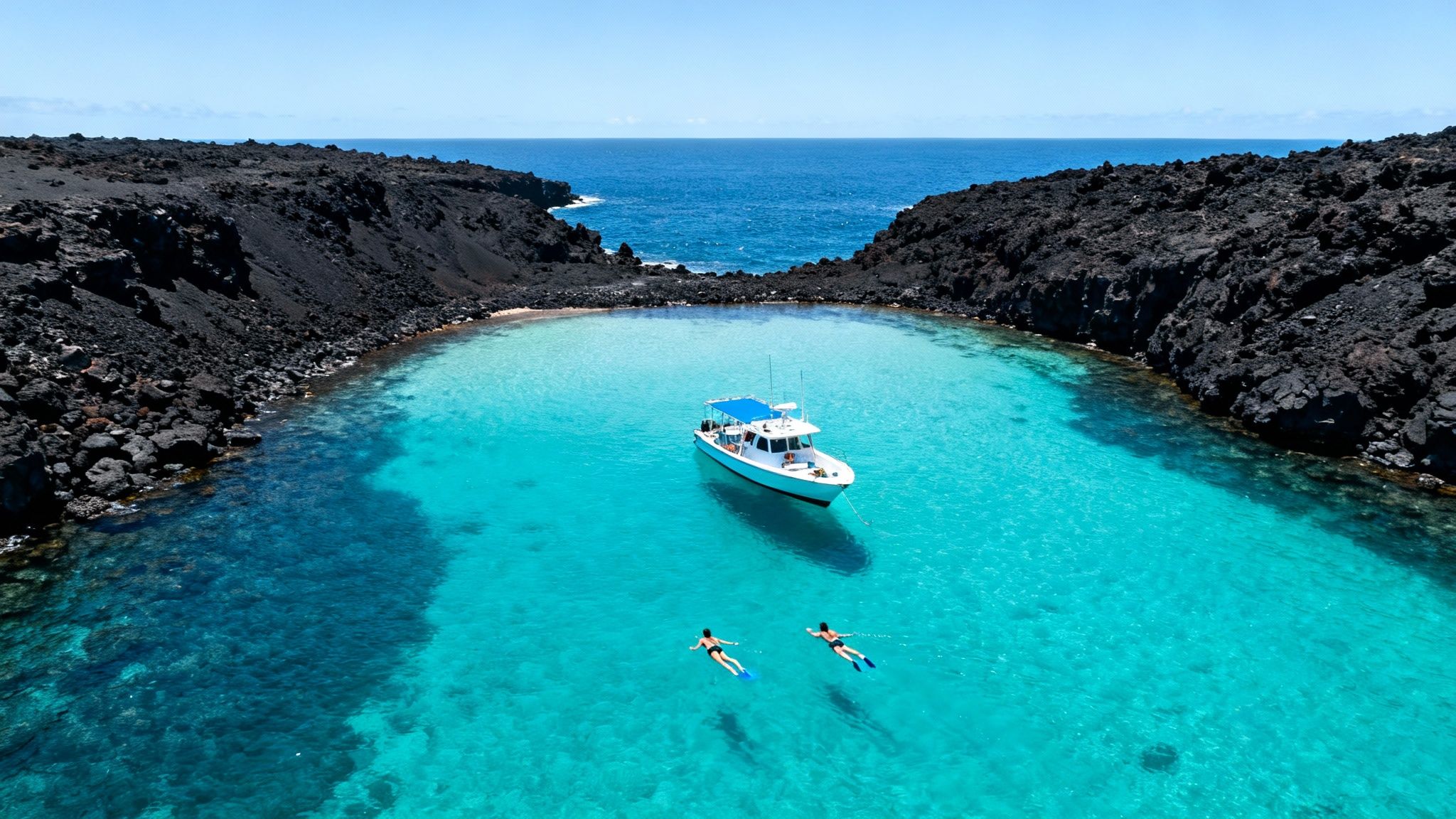 Aerial view of a boat in a vibrant turquoise bay with volcanic rocks and two snorkelers.