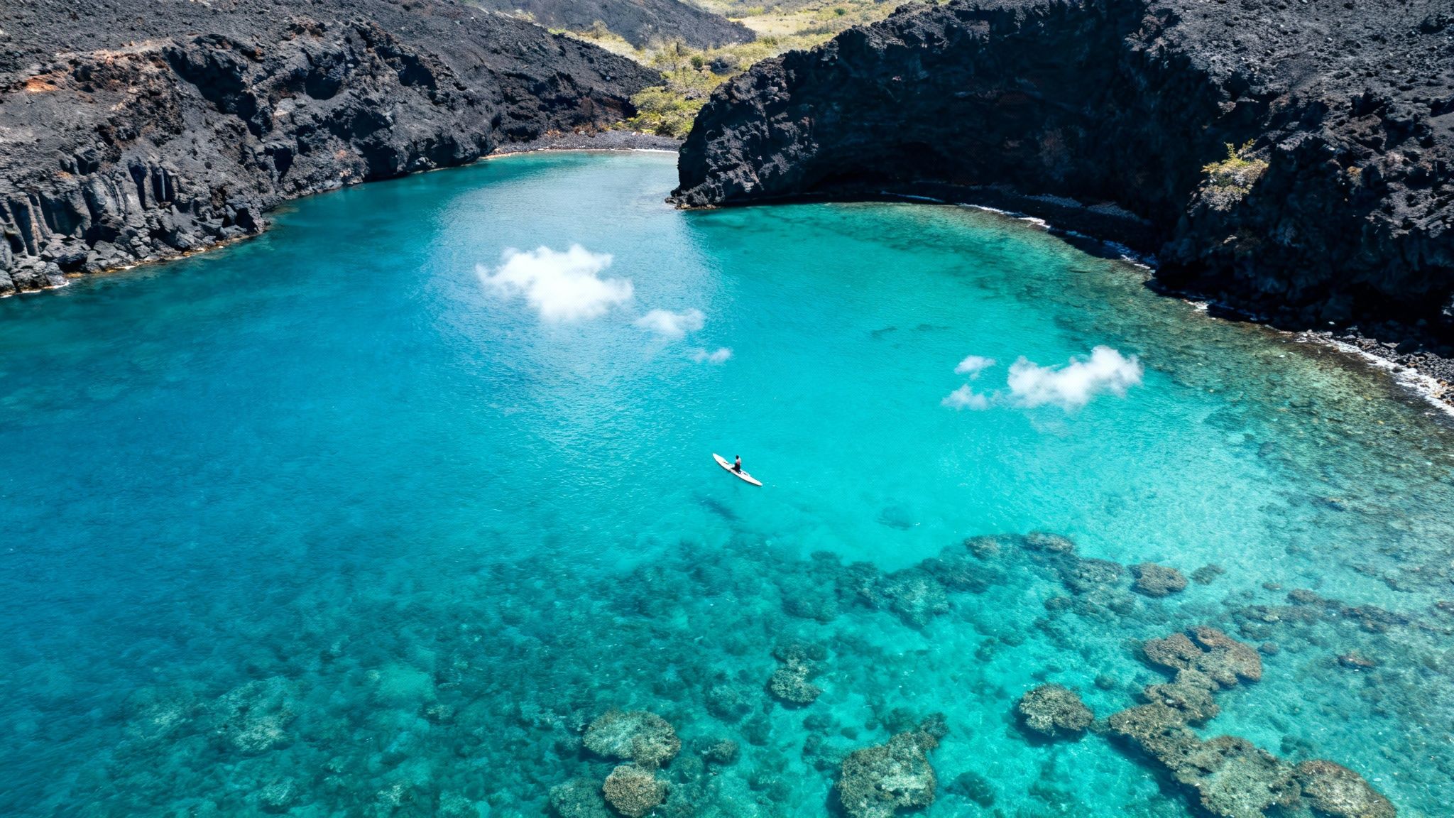 Aerial view of a paddleboarder in turquoise Kealakekua Bay, Hawaii, surrounded by volcanic rock formations.