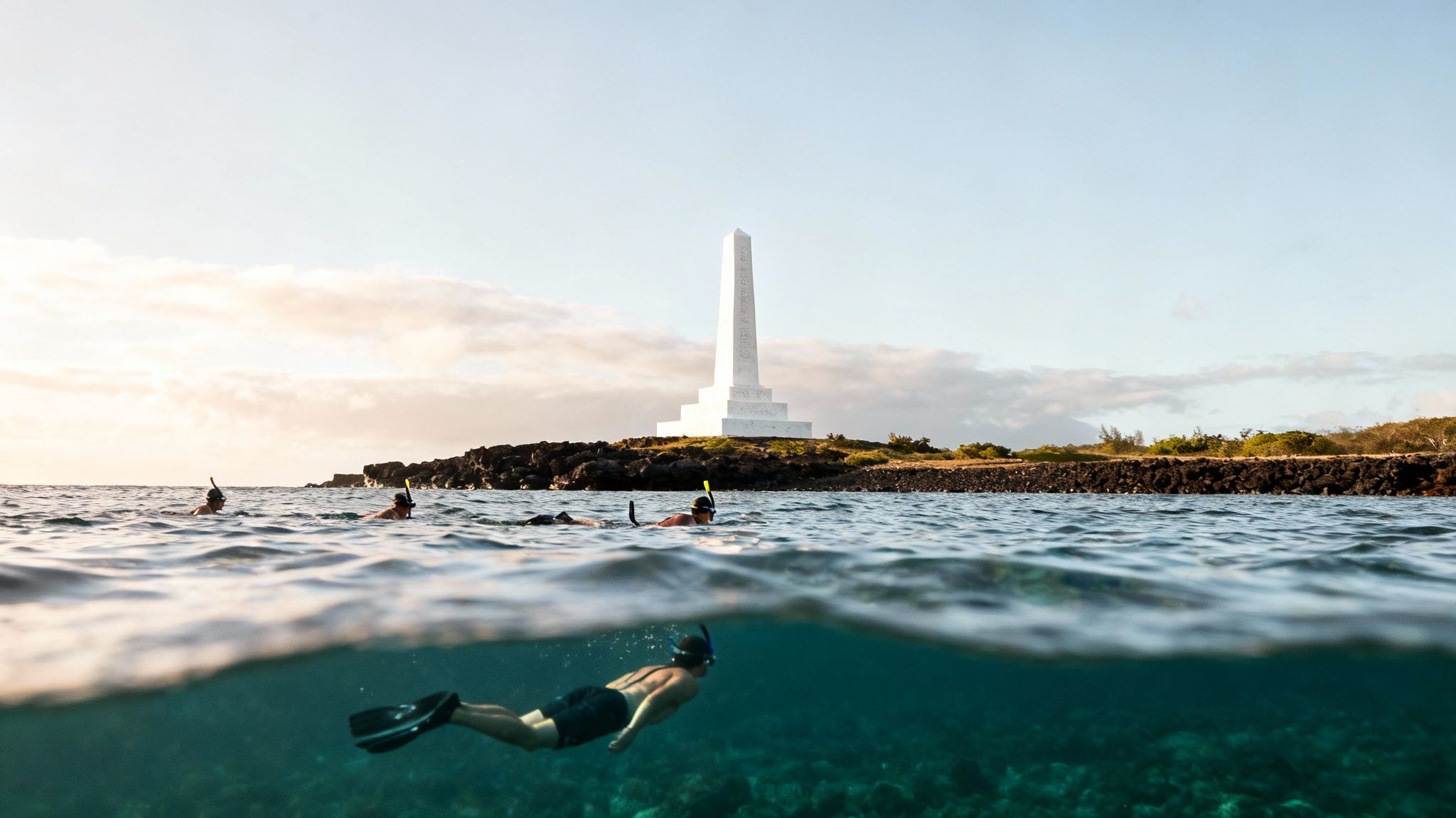 Snorkelers explore Kealakekua Bay near Captain Cook monument at sunset, showcasing an over-under split view.