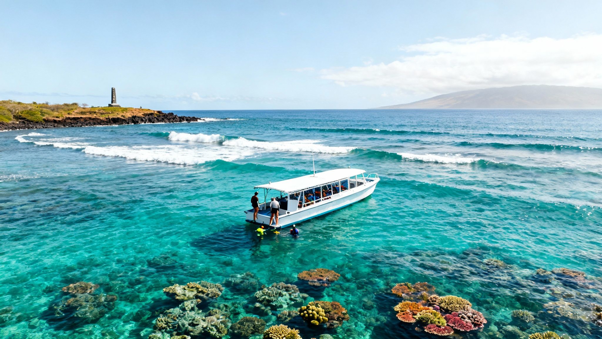 A white tour boat with snorkelers in clear turquoise ocean water over a vibrant coral reef, with a monument on a rocky shore.