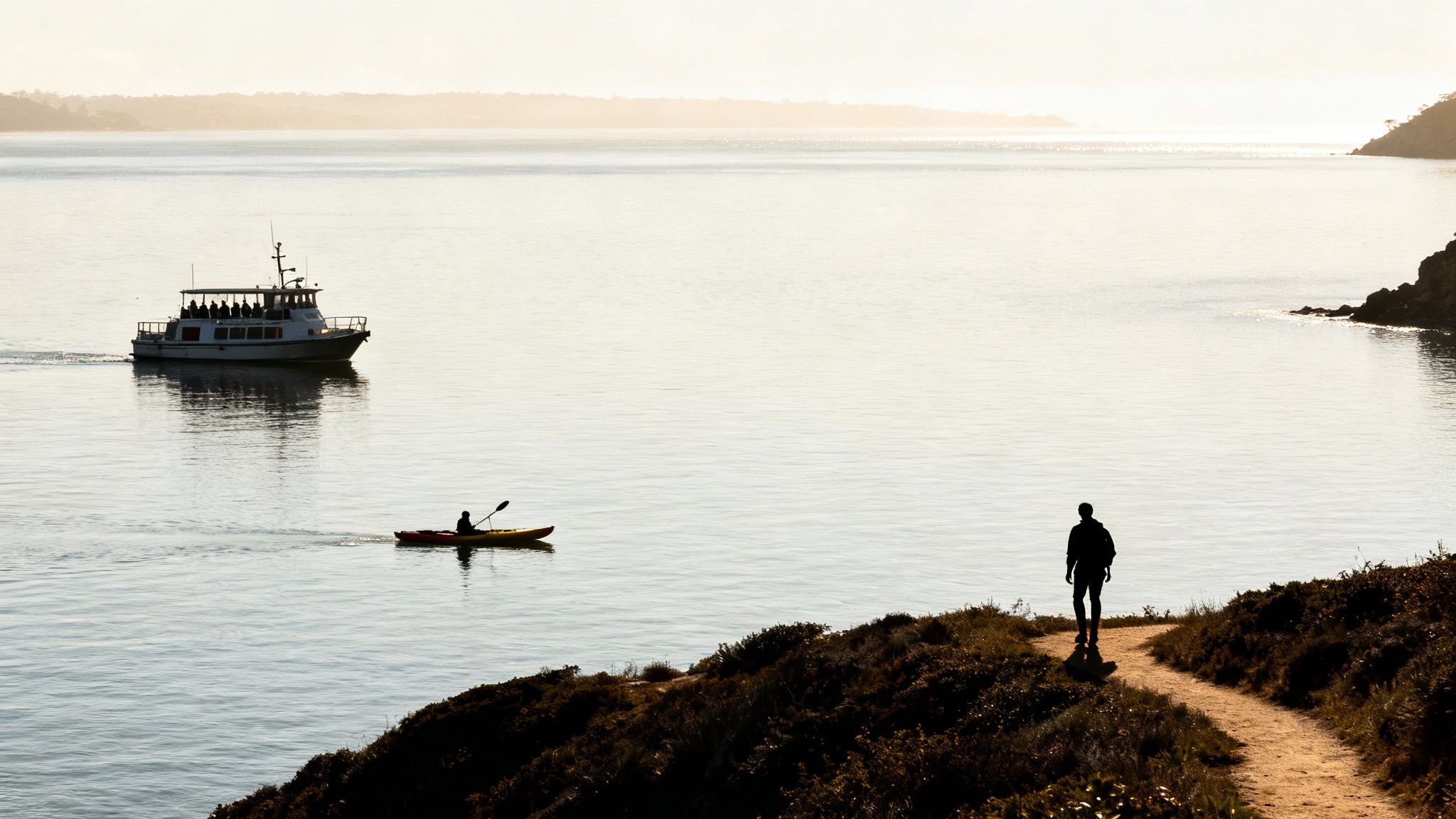 Ferry boat and kayaker on calm coastal waters with silhouetted hiker walking shoreline path