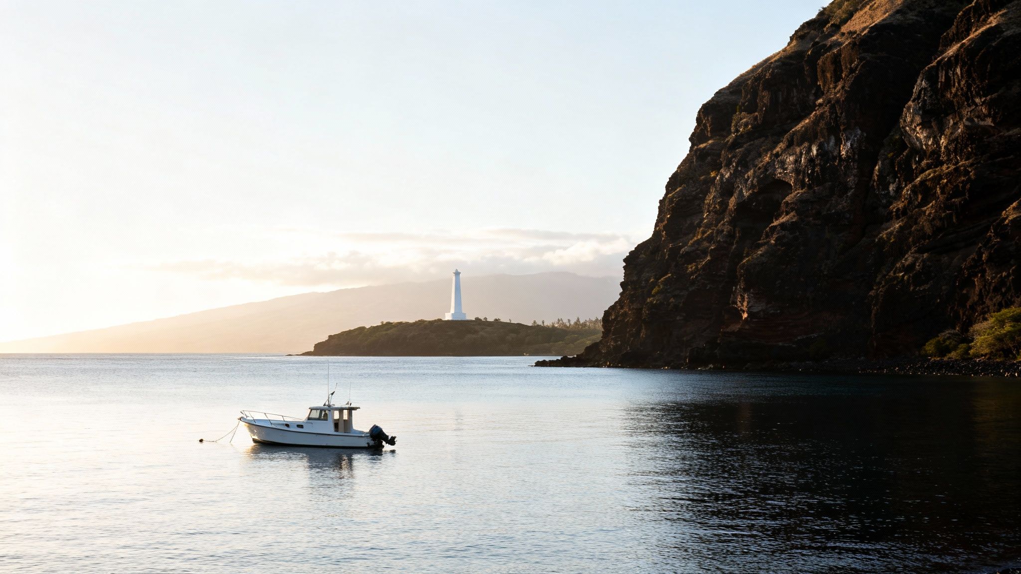 A white boat anchored in calm water with a lighthouse on a distant shore and a dark cliff.