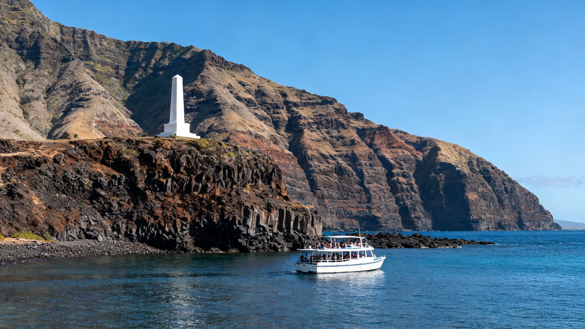 A white tour boat with people sails in clear blue waters near a monumental cliff and mountain.