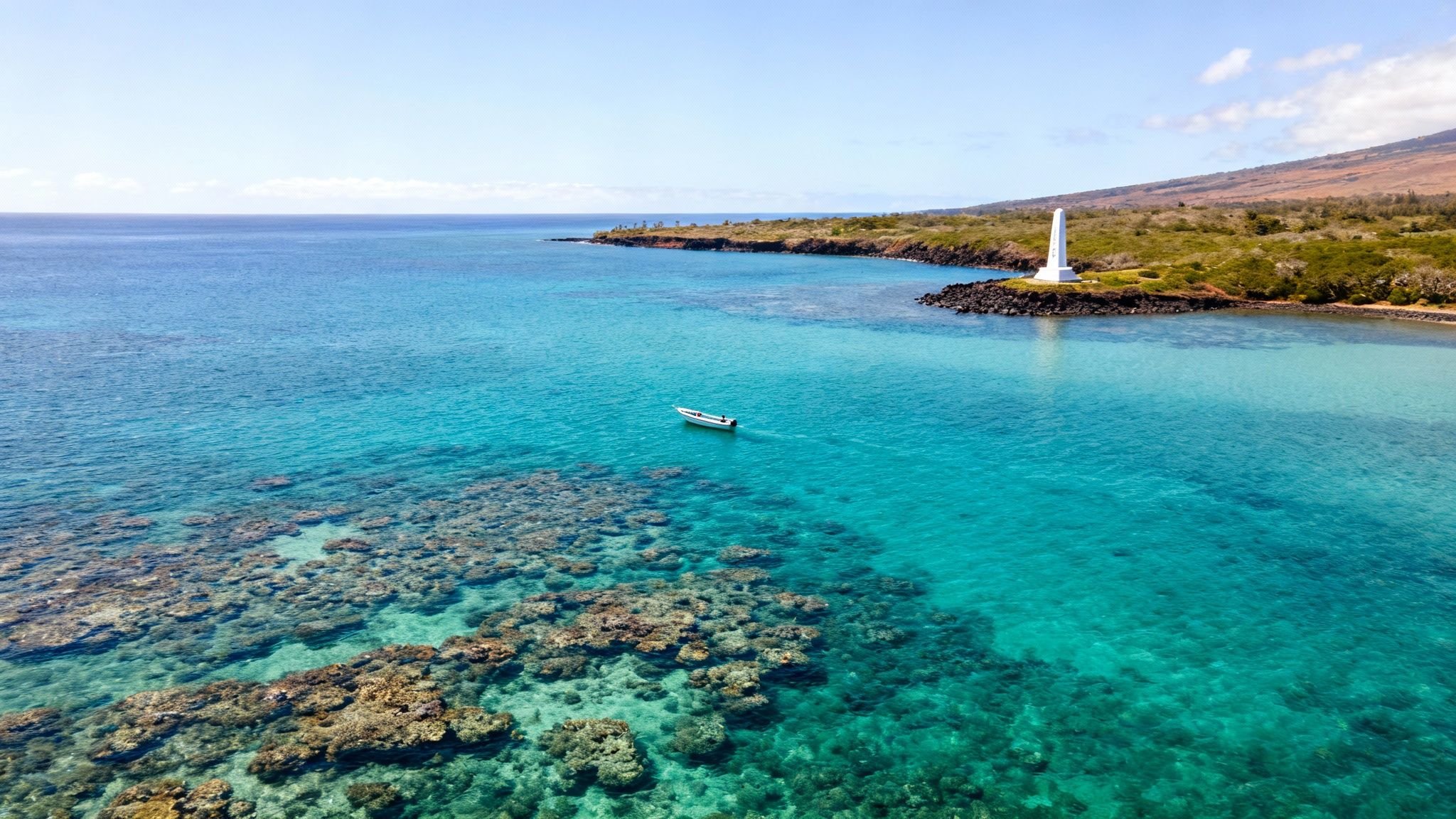 Aerial view of Kealakekua Bay with a white monument, boat, and vibrant coral reef.