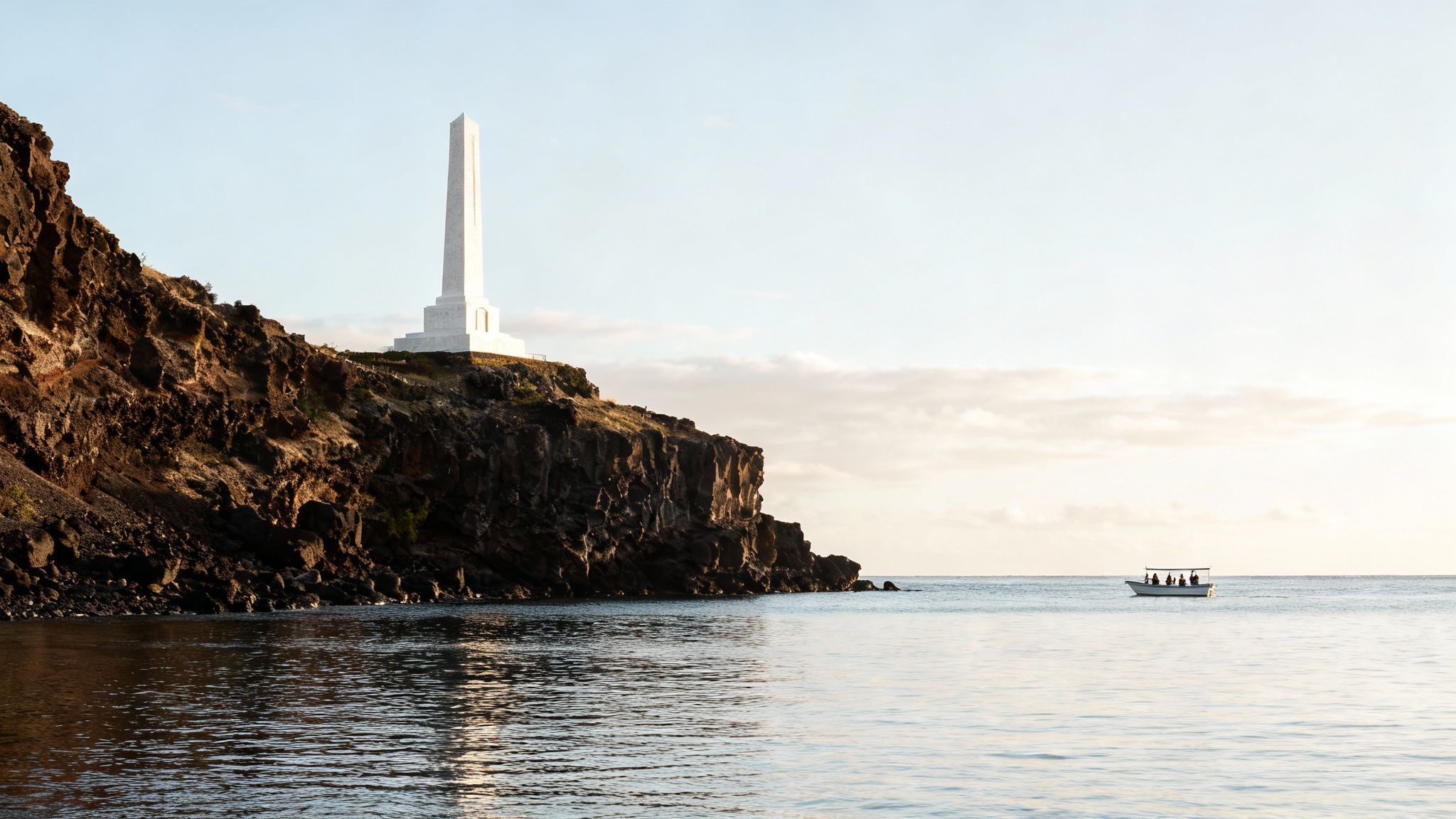 A white obelisk monument stands on a rocky cliff above calm ocean waters with a small boat in the distance.