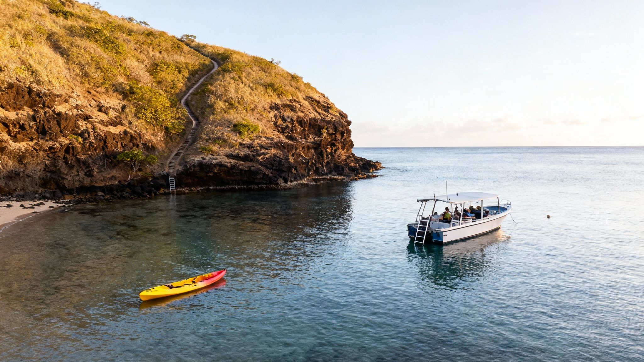 Scenic view of a tour boat and kayak in calm blue water near a golden cliff with a winding staircase.