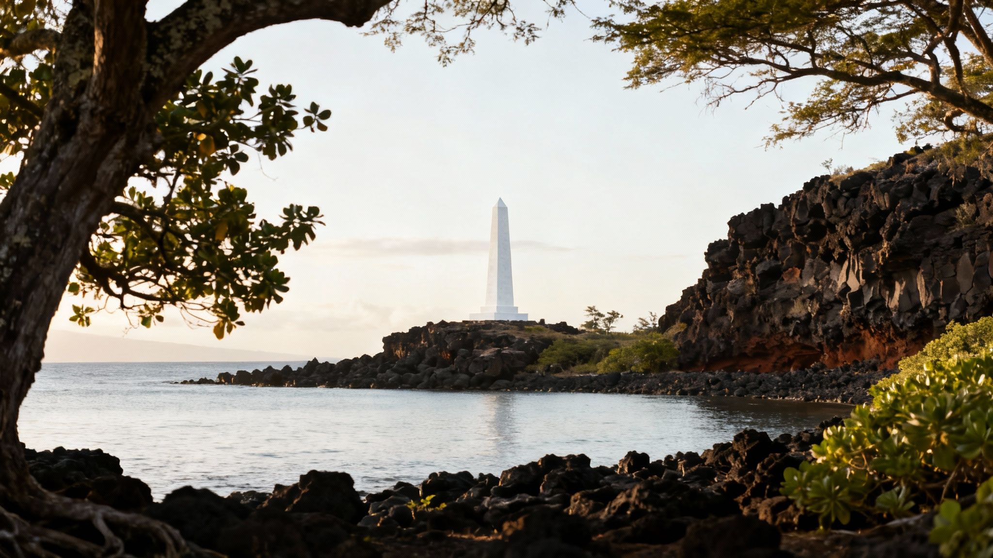 White obelisk monument on a rocky Hawaiian coast with calm water, framed by lush trees.