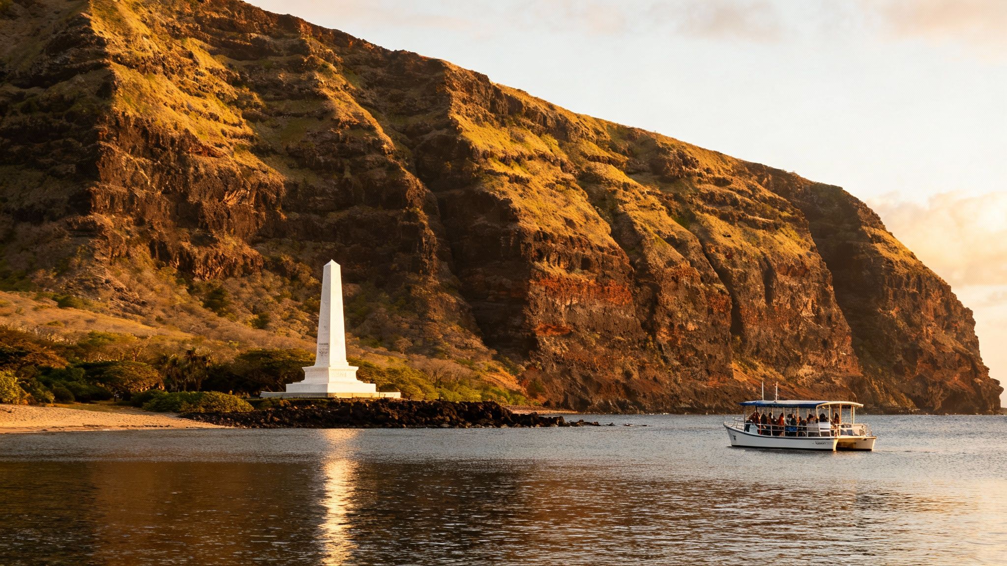 A tour boat passes the white Captain Cook Monument on Kealakekua Bay at golden hour.
