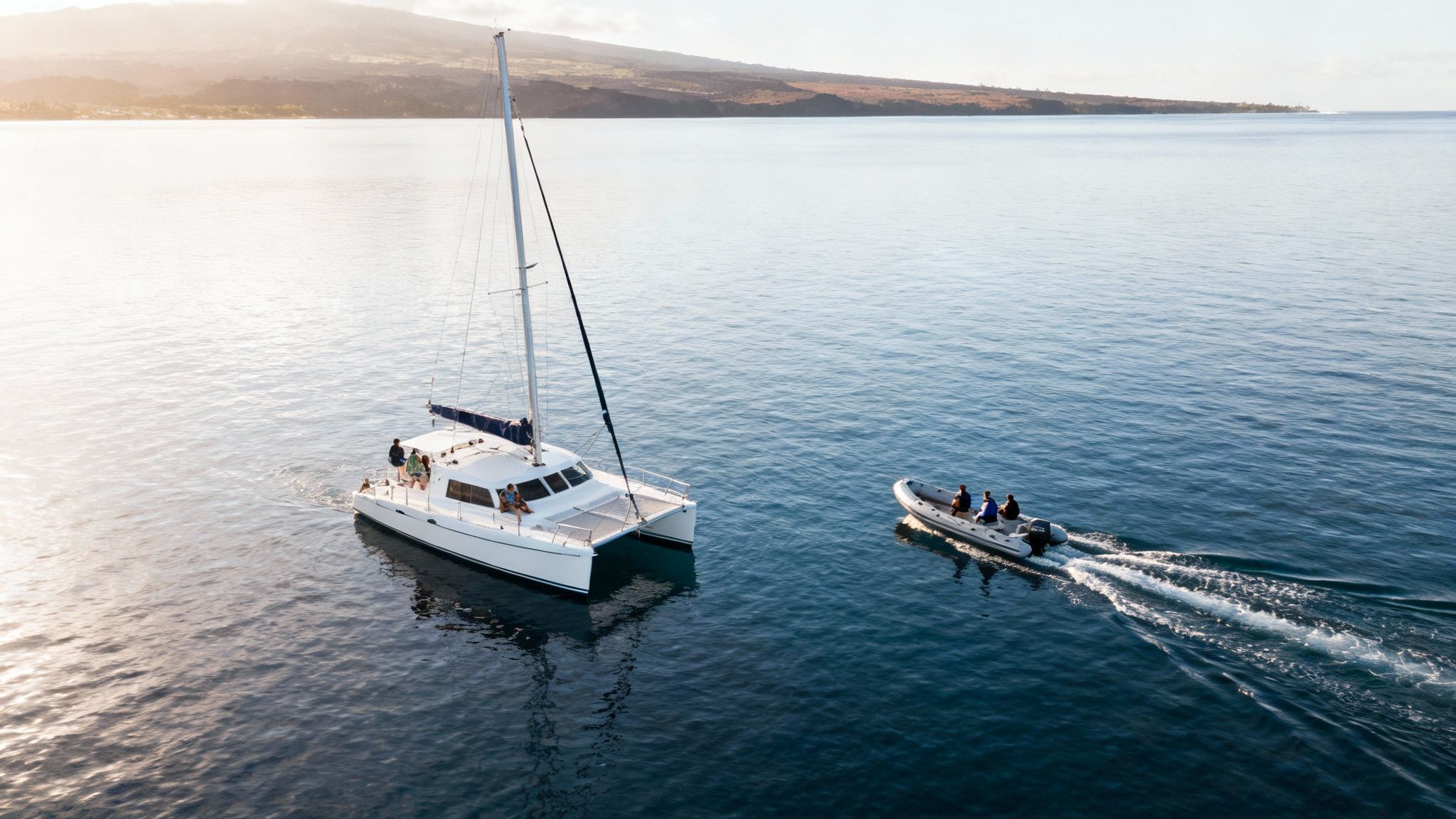 Aerial view of a white catamaran and inflatable boat with people sailing on calm ocean.
