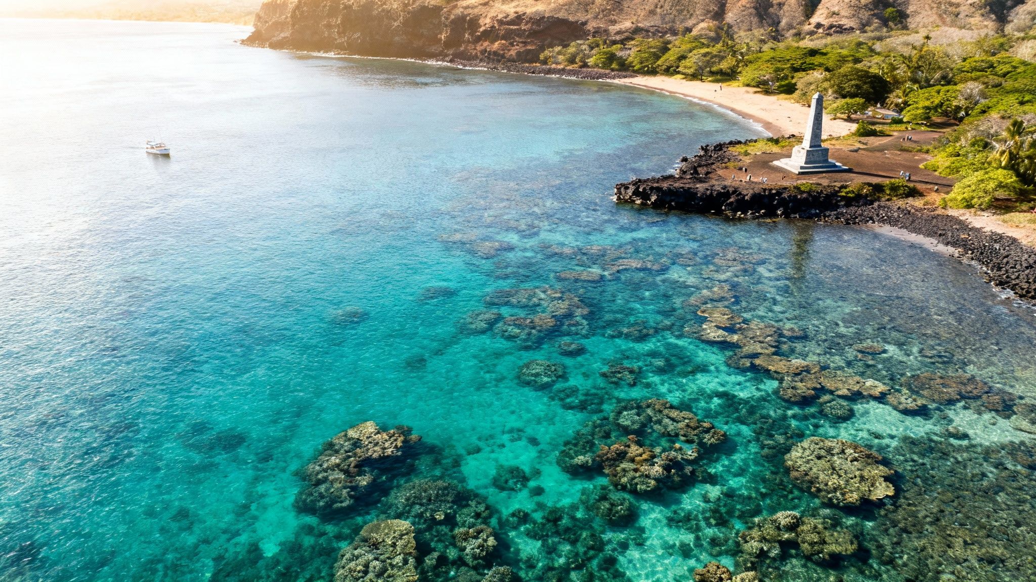 Aerial view of clear turquoise water, vibrant coral reefs, a sandy beach, and the Captain Cook monument.