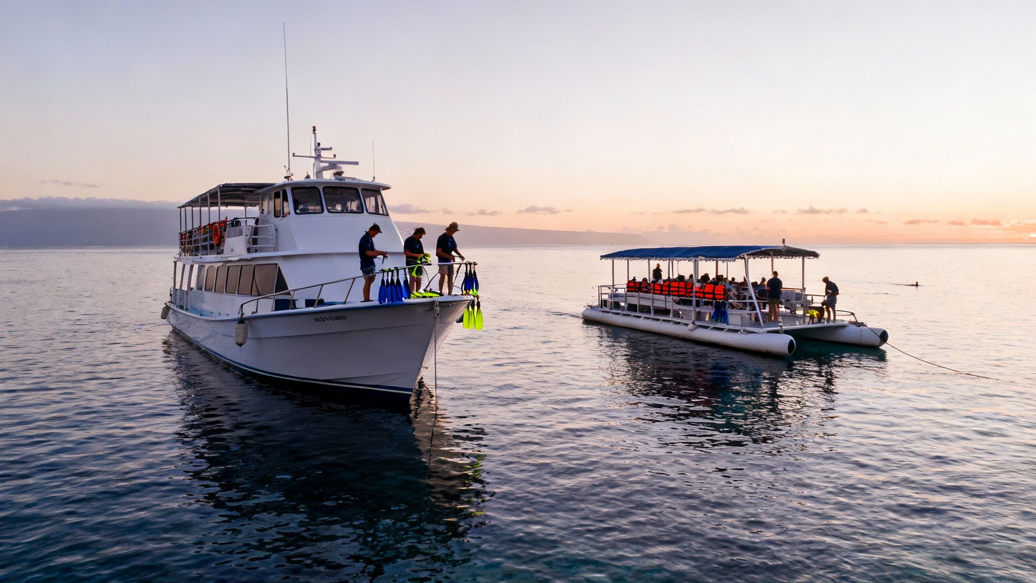 Two boats on the ocean at sunrise, one with snorkelers and the other with passengers.