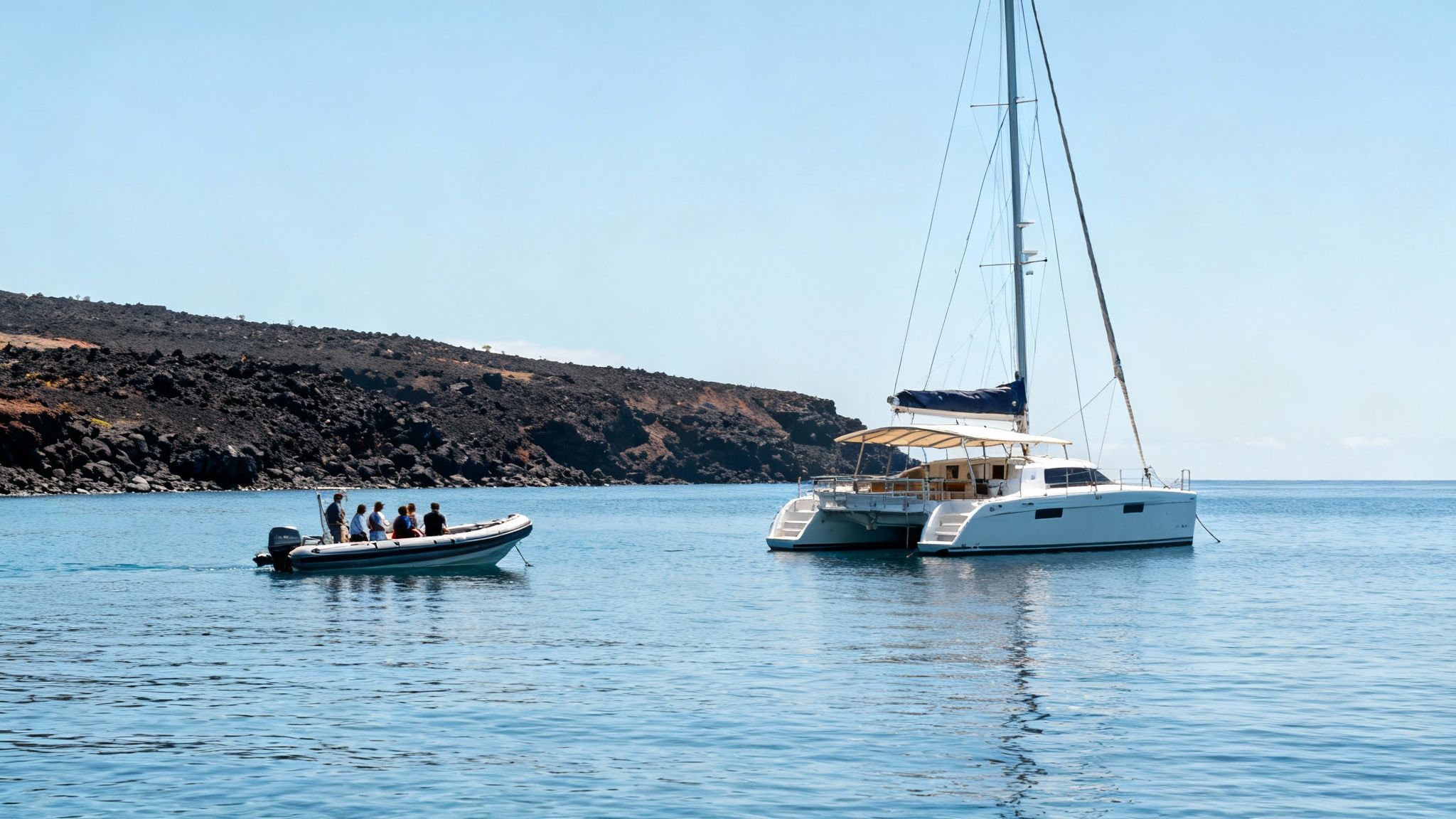 White catamaran yacht anchored near volcanic coastline with small dinghy boat carrying passengers