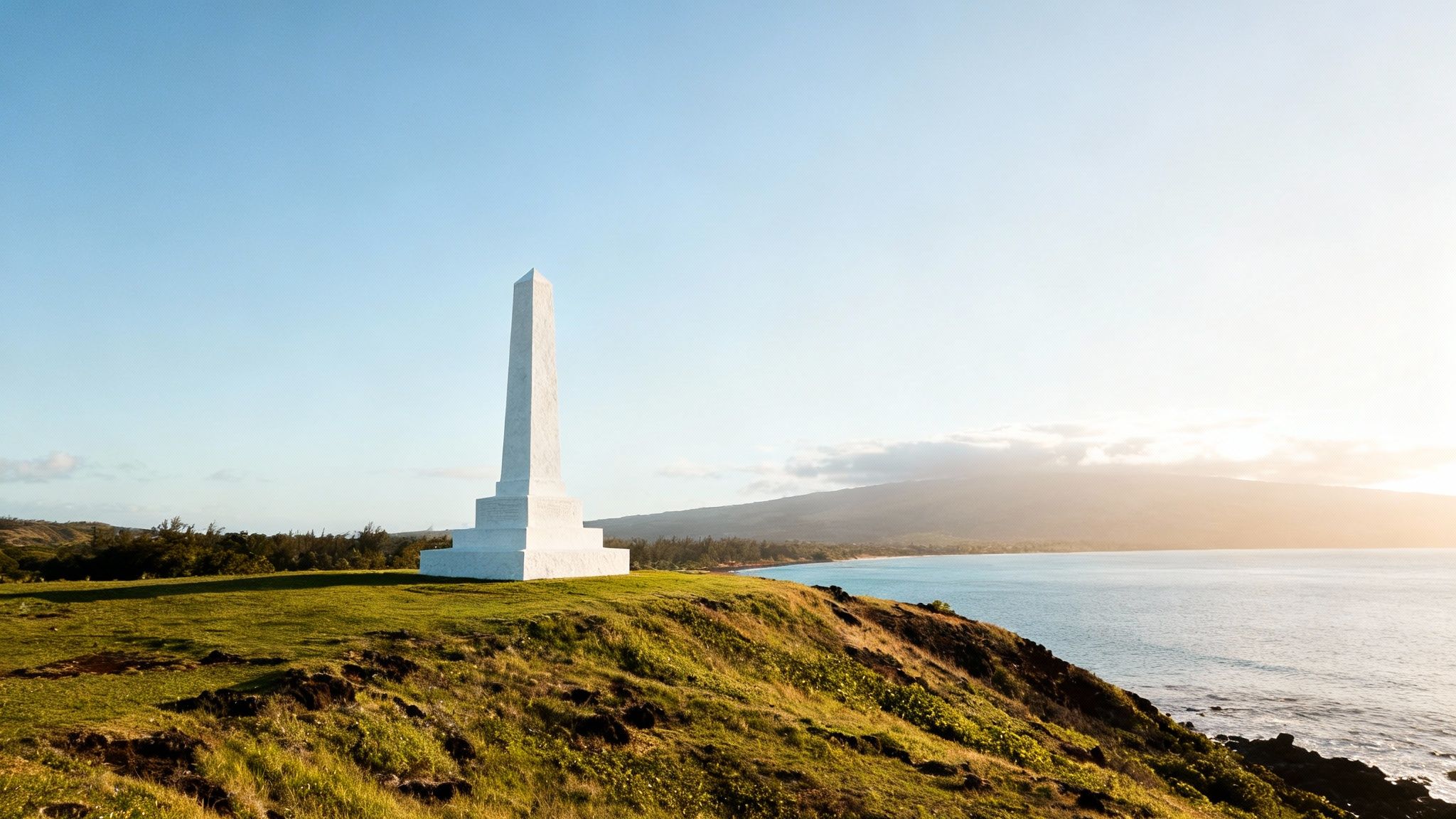 The white Captain Cook Monument stands tall against the green cliffs of Kealakekua Bay.