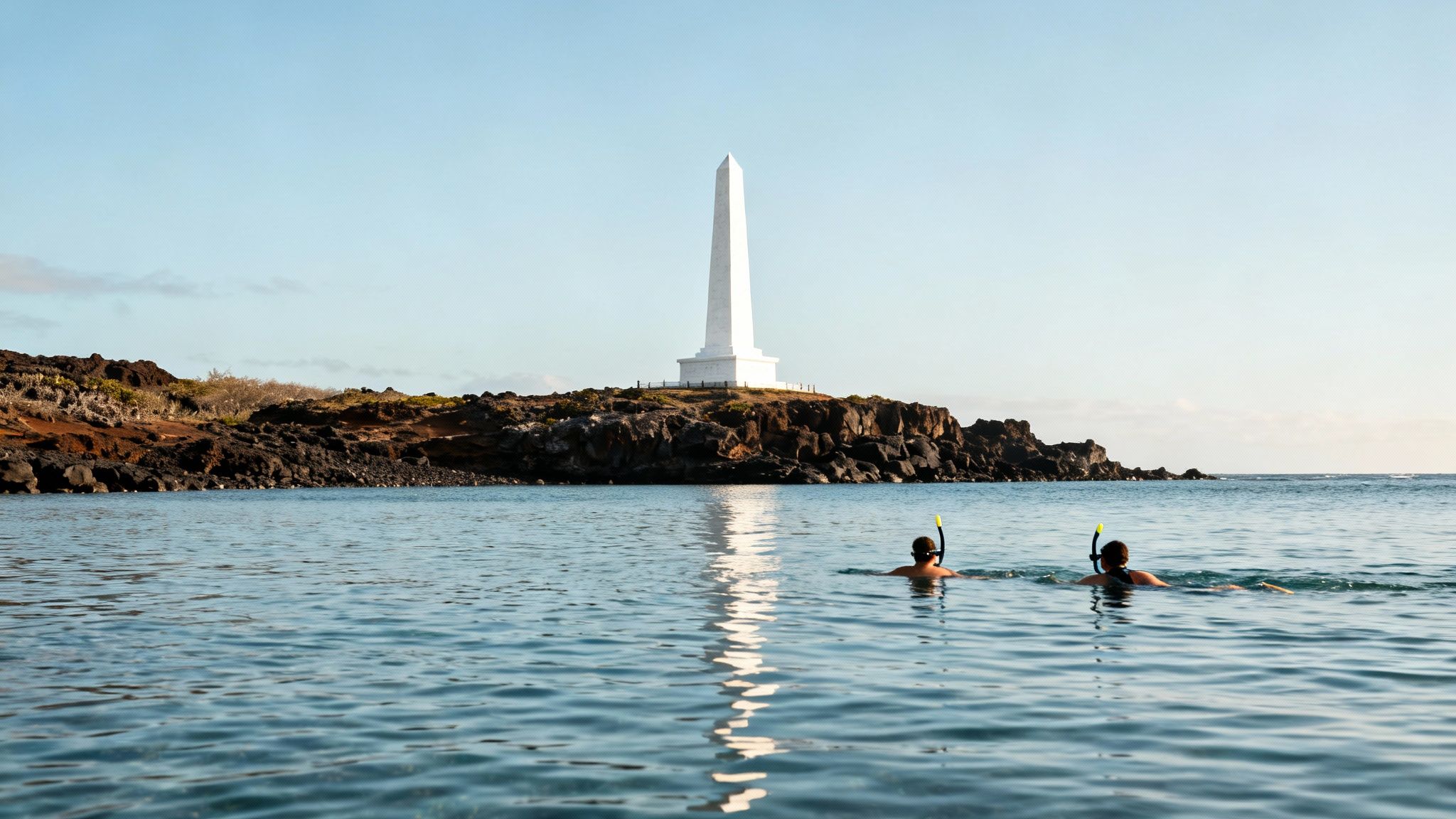 Two people snorkel in the ocean with a white obelisk monument on a rocky shore in the distance.