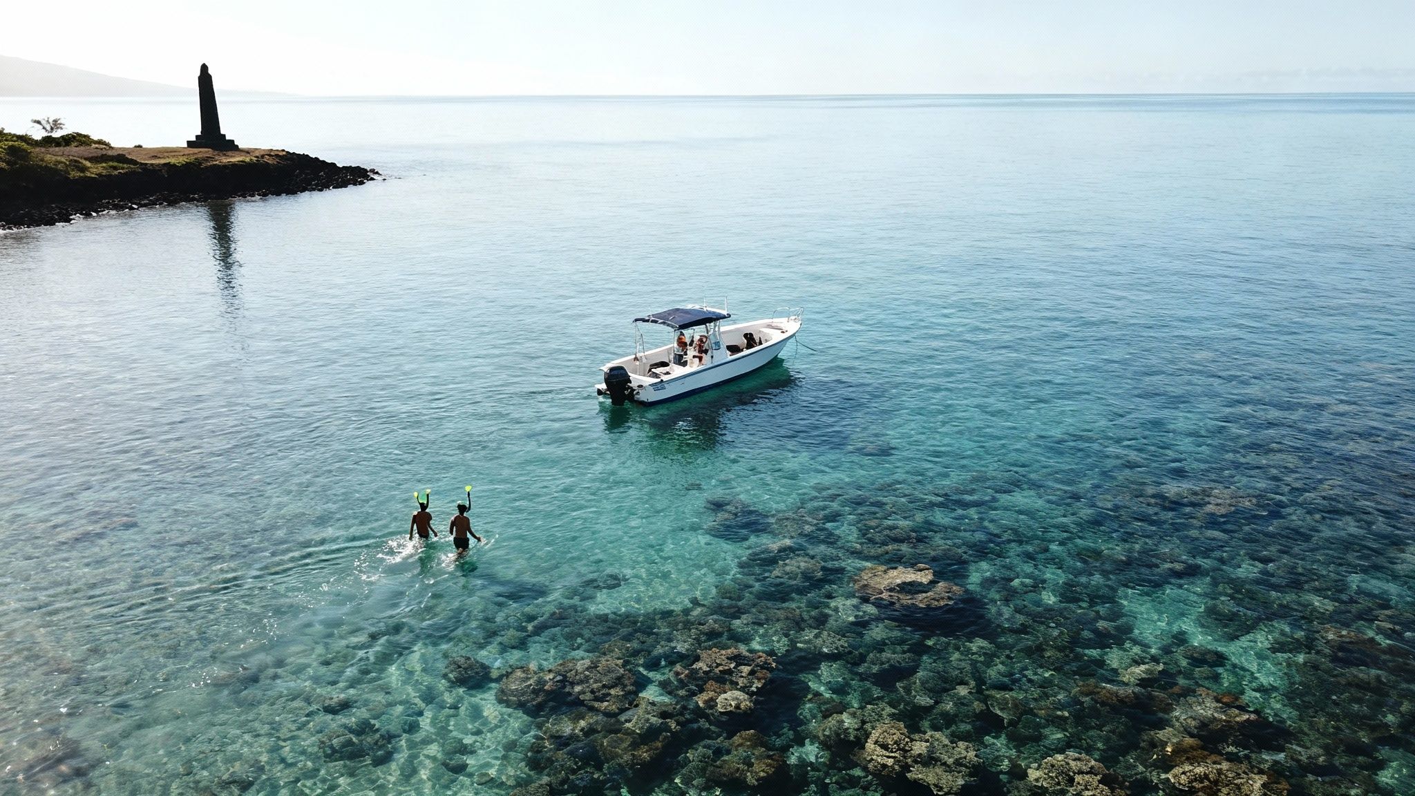 Two people snorkeling in clear turquoise water near a boat, a lighthouse, and underwater coral.