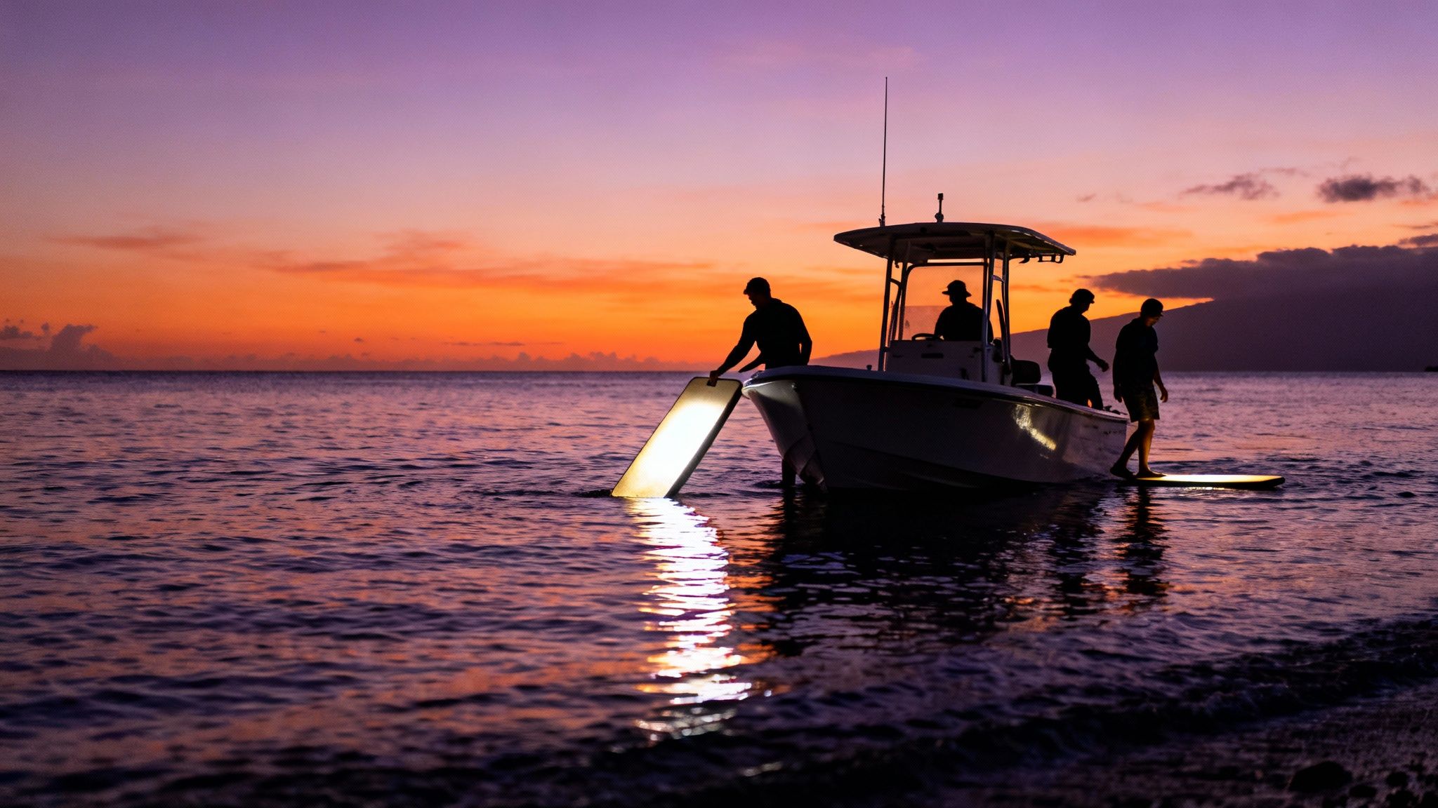 Silhouetted people from a boat at dusk, using underwater lights for night snorkeling.