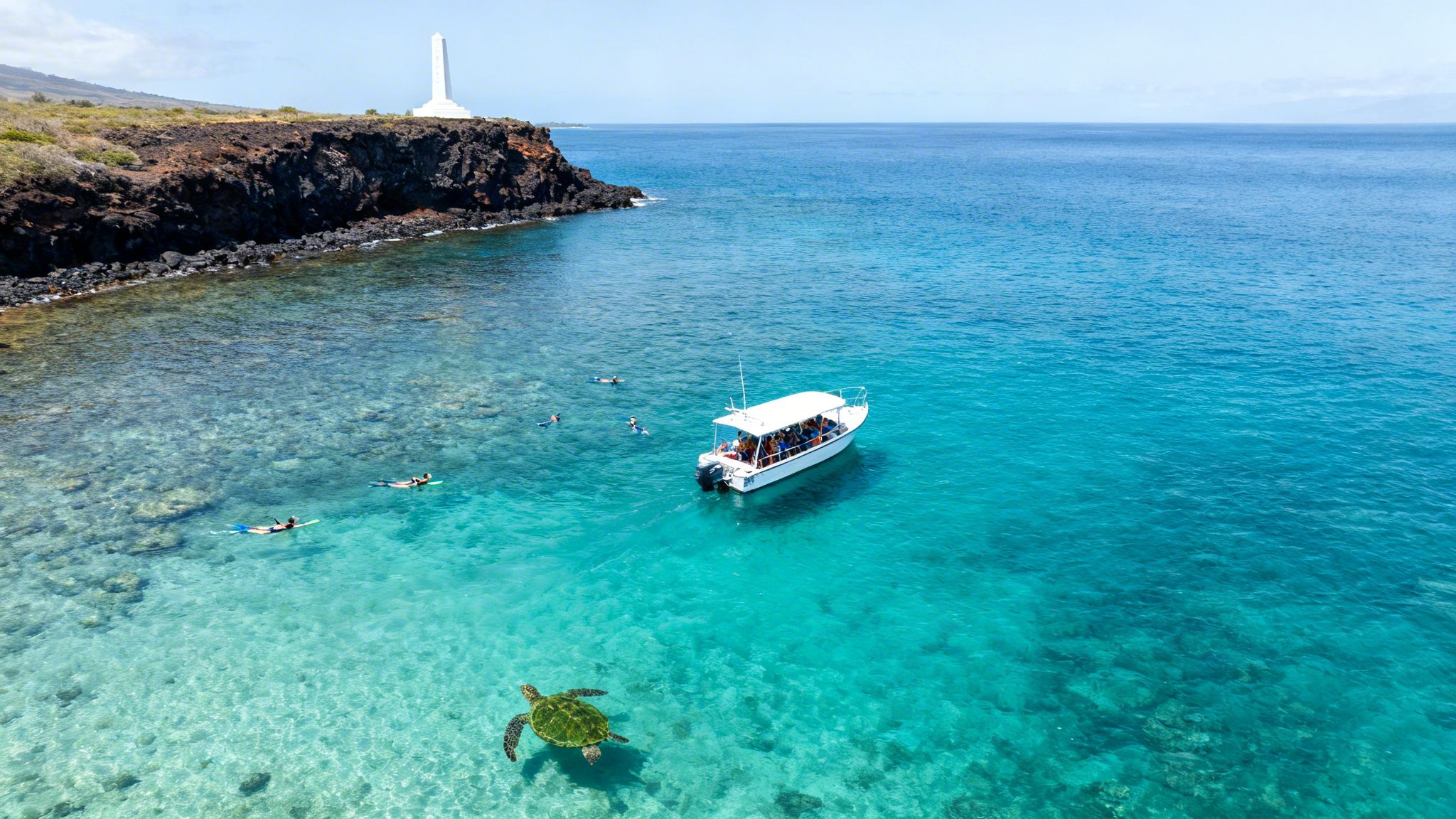 Aerial view of a boat, snorkelers, and a sea turtle in clear blue Hawaiian waters near a rocky coast.
